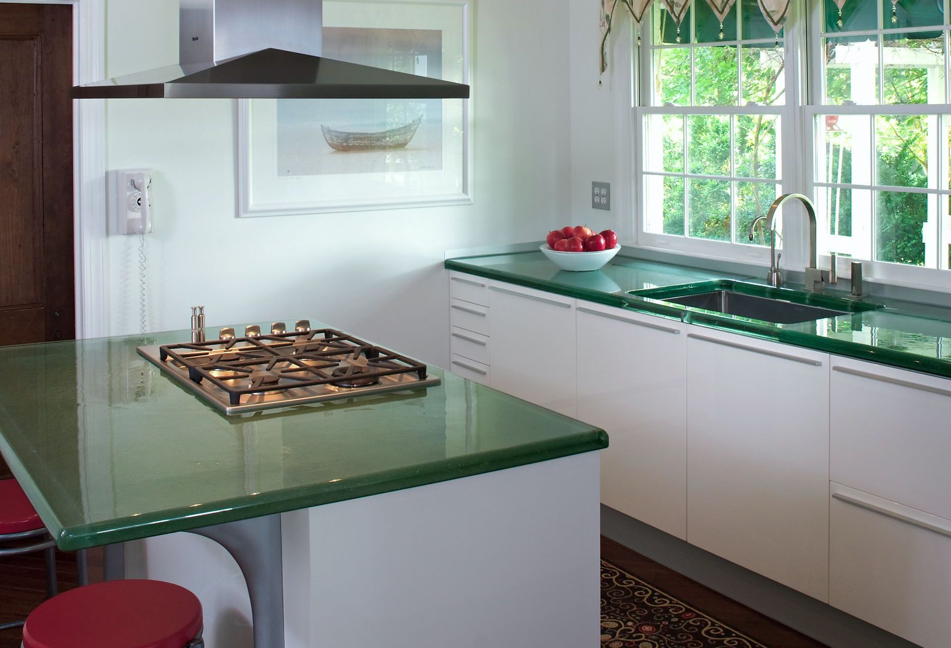 Modern kitchen with green countertops, gas cooktop island, white cabinets, and large window sink