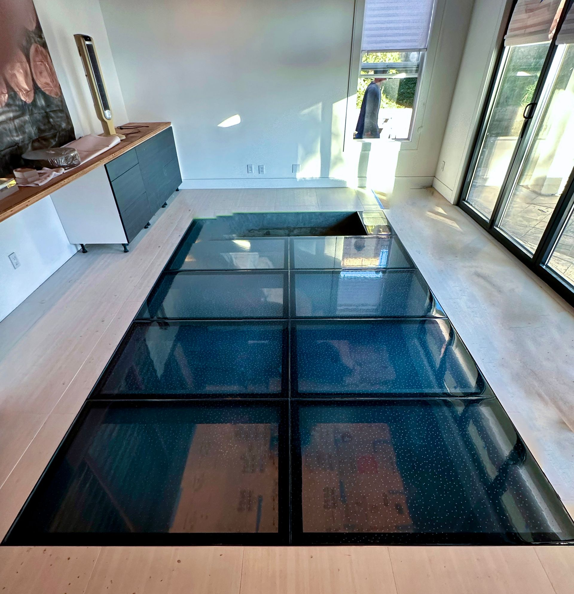 Glass floor panels in a bright room with a view to the outside and cabinetry along the wall.