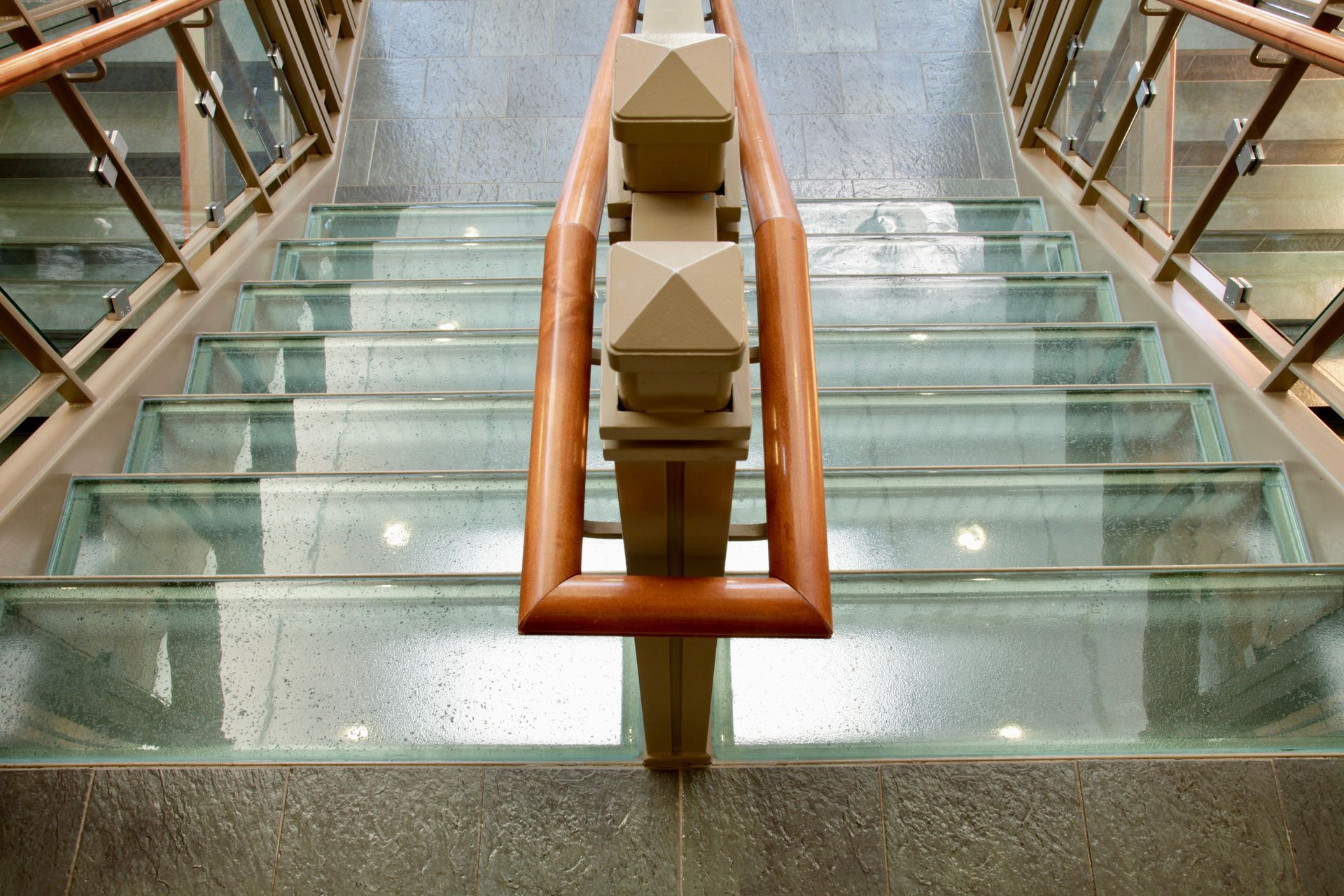 Glass staircase with wooden handrails and decorative supports.