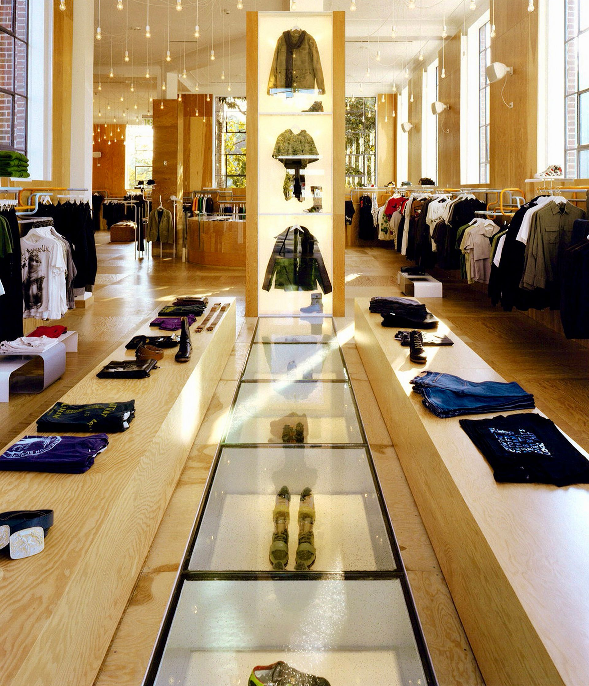 Clothing store interior with wooden displays, glass walkway, and merchandise on racks.