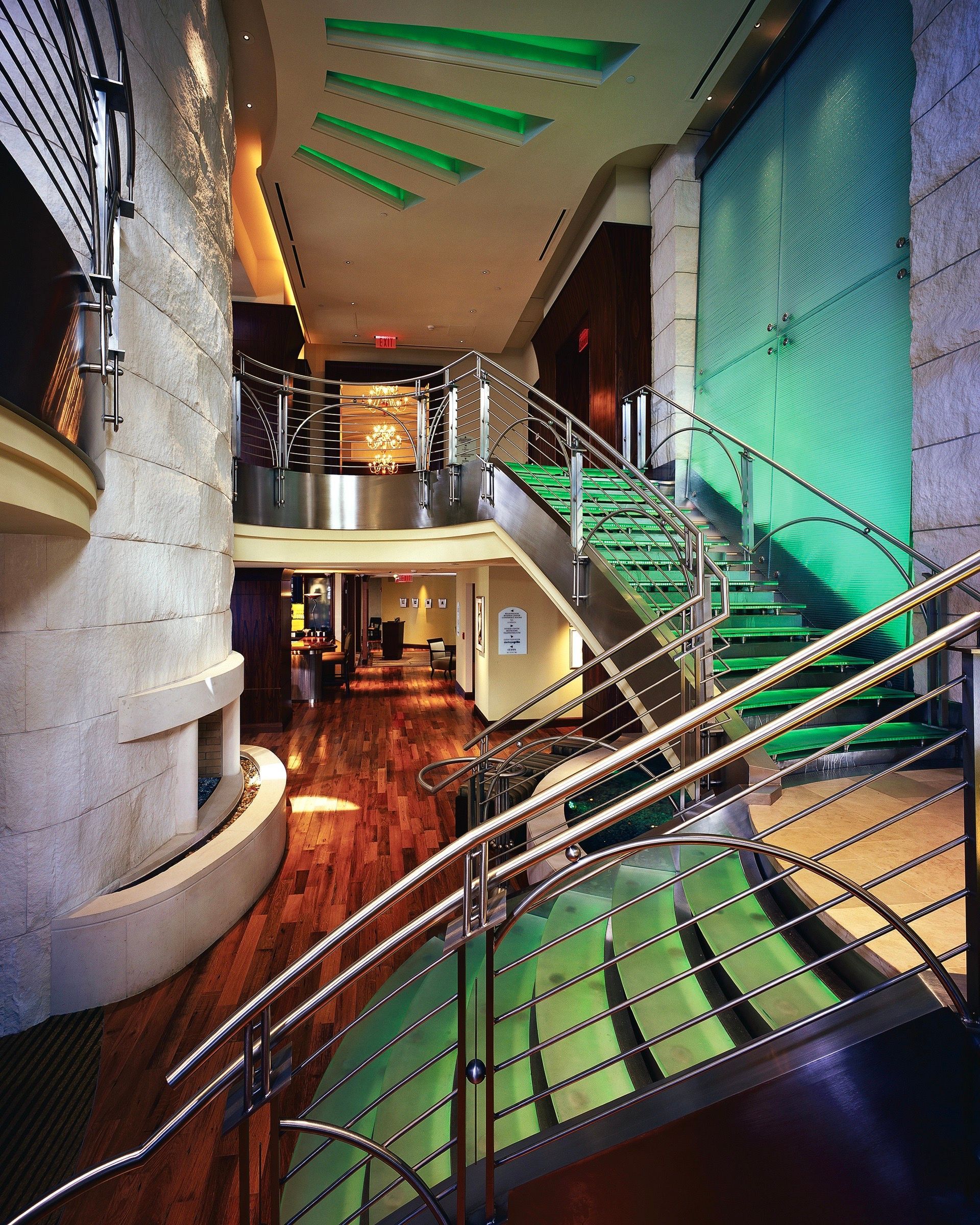 Modern atrium with curved staircase, green-lit steps, and balconies in a sleek interior.