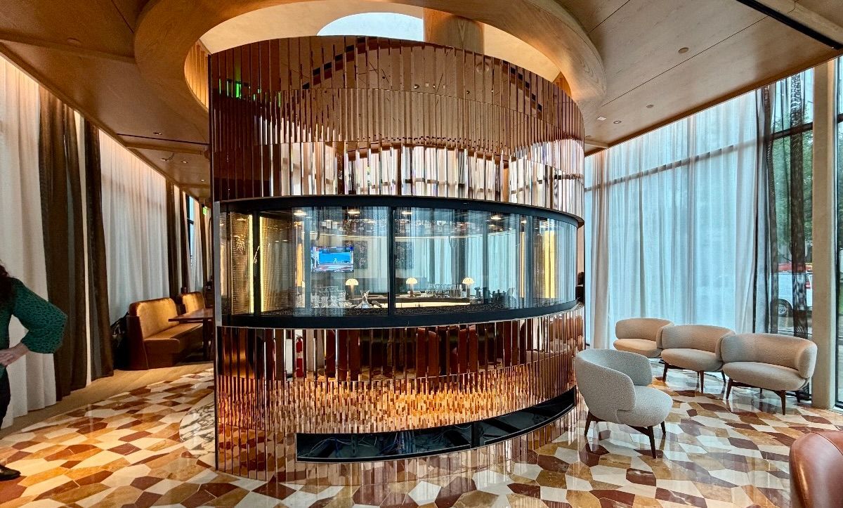 Modern hotel lobby with a circular glass centerpiece, warm wood ceiling, and upholstered seating area