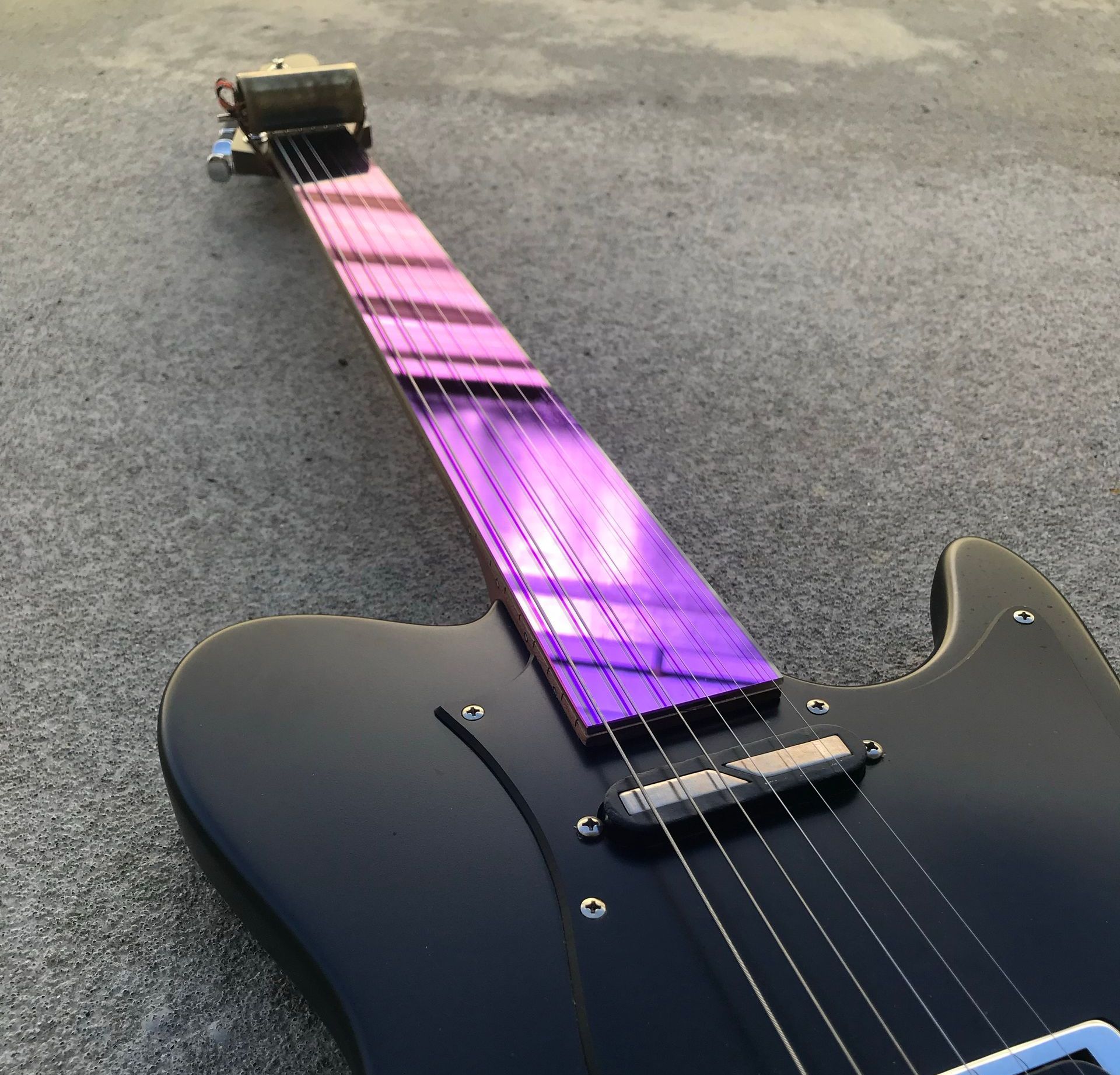 A black electric guitar with a purple neck sits on a carpet