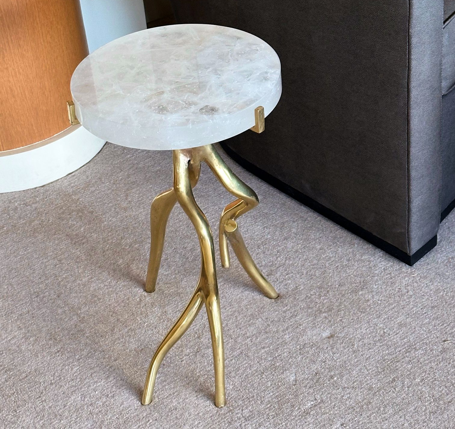 Gold twig-legged side table with a round, white cast glass top on beige carpet.