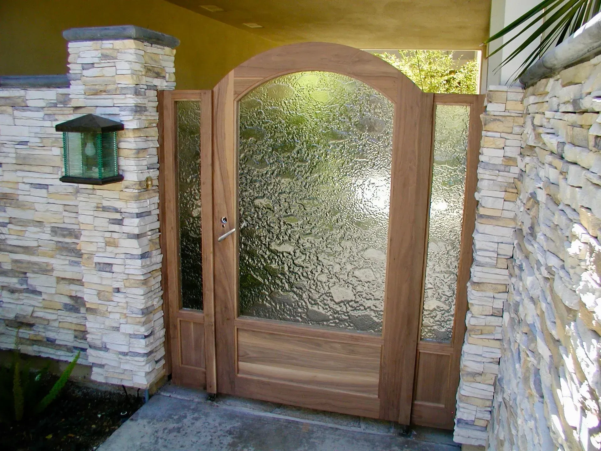 Wooden gate with textured glass panels, set between stone pillars with a lantern.