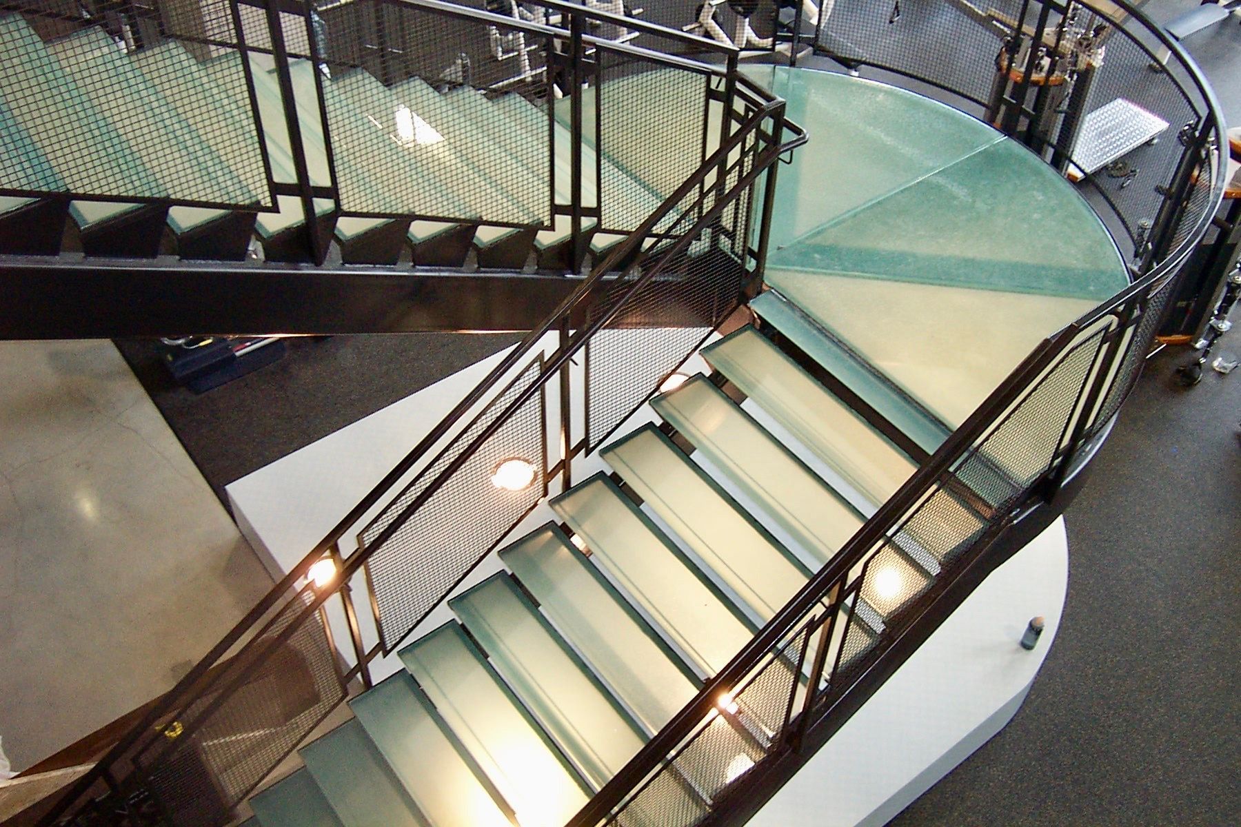 A modern, glass staircase with black metal railings curves upward.