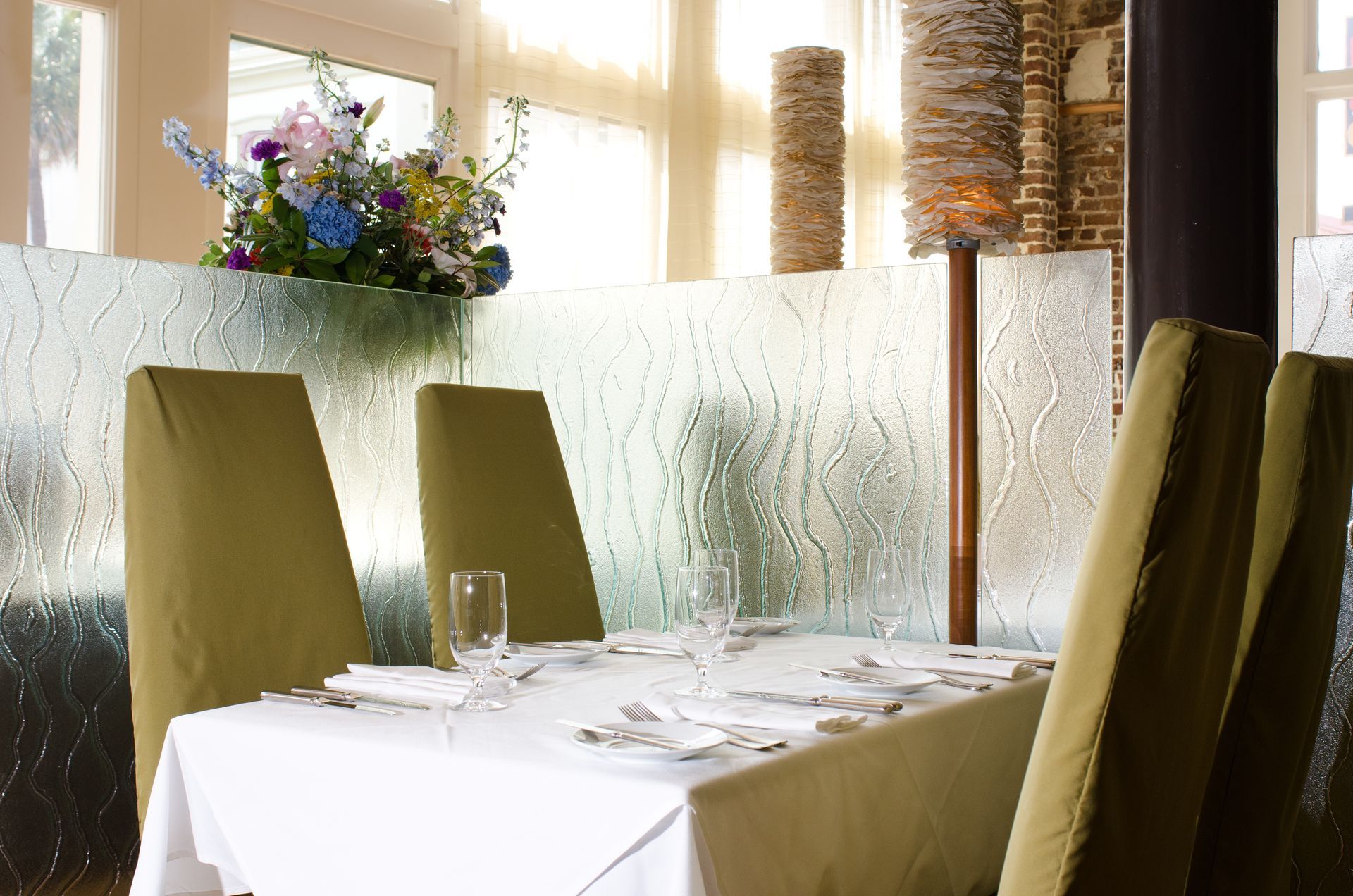 Elegant restaurant table with white cloth, olive chairs, and a floral centerpiece by a frosted window