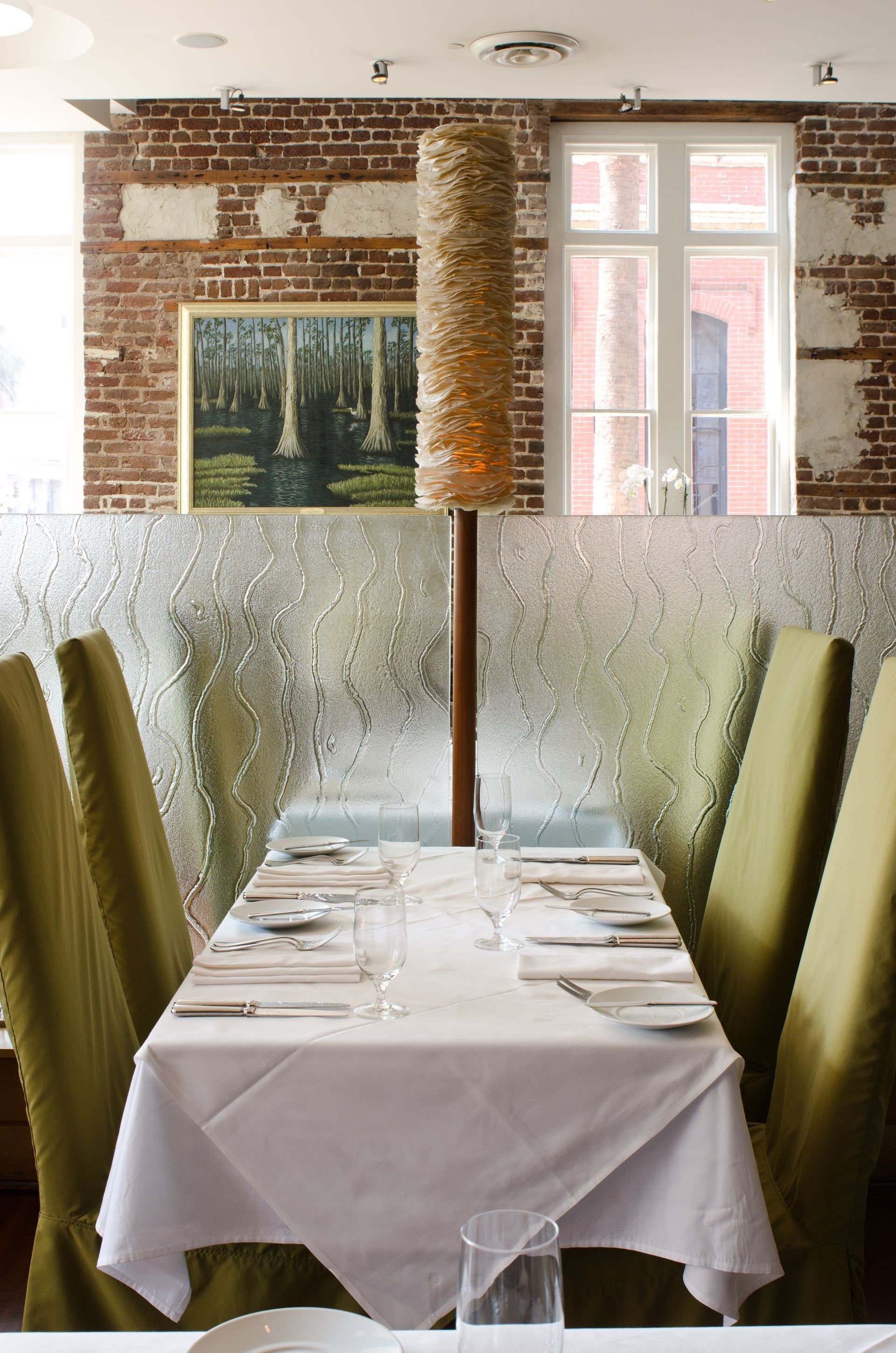Elegant restaurant table set by a frosted glass window, with white linens and green chairs.