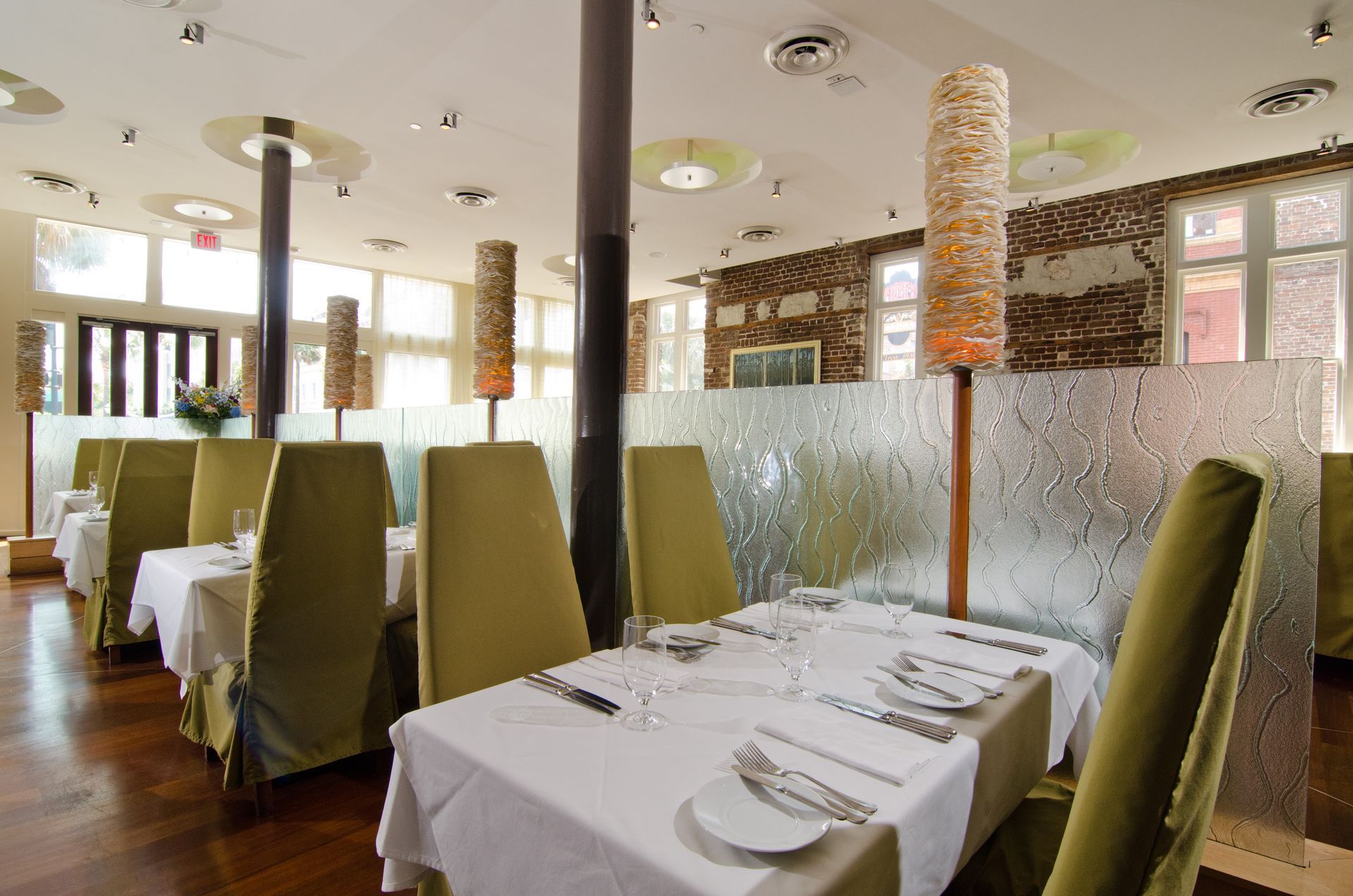 Modern restaurant dining area with set tables, green chairs, and frosted glass partitions