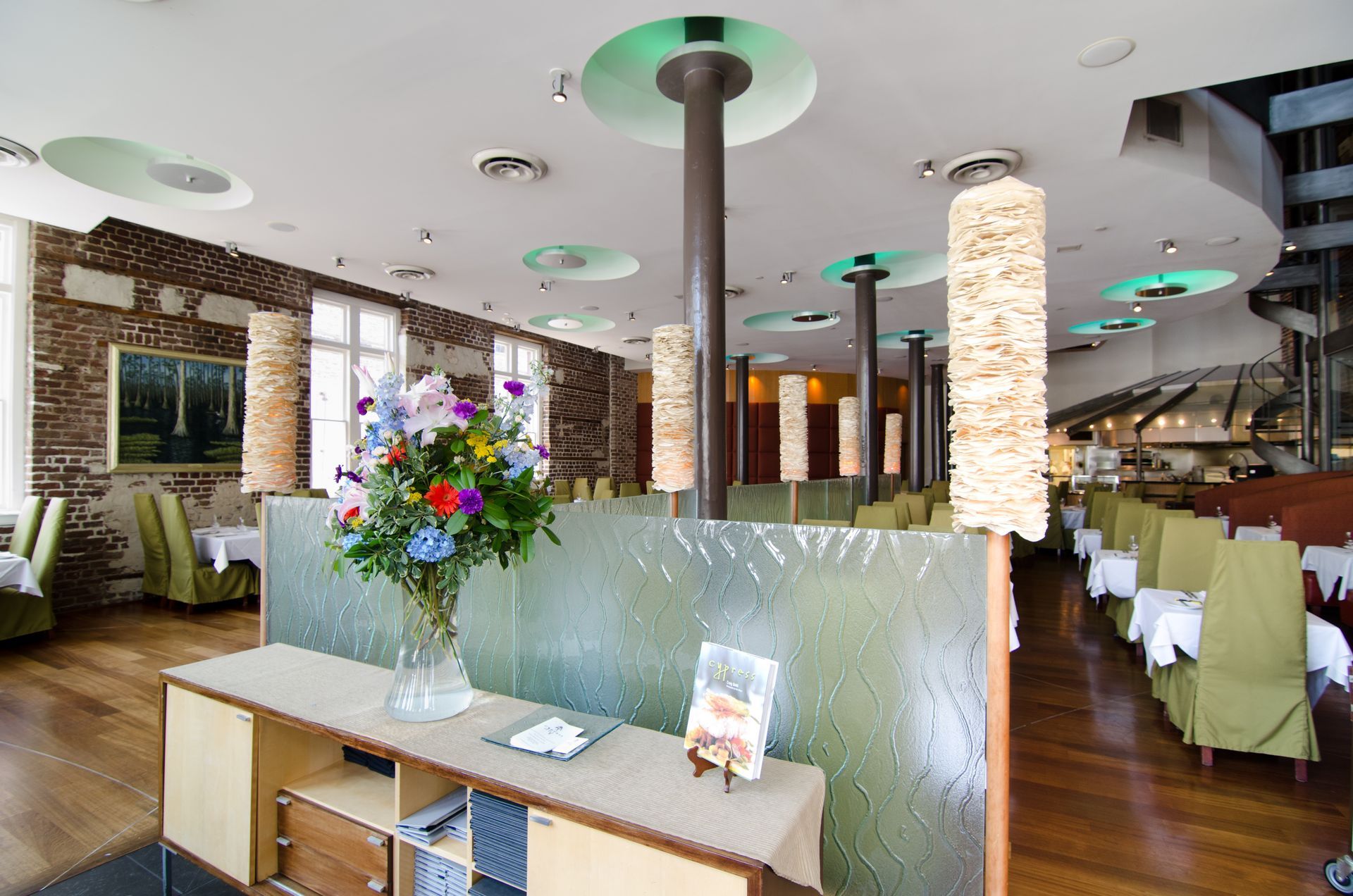 Stylish restaurant interior with white chairs, stone columns, wooden floors, and a flower arrangement at the host stand