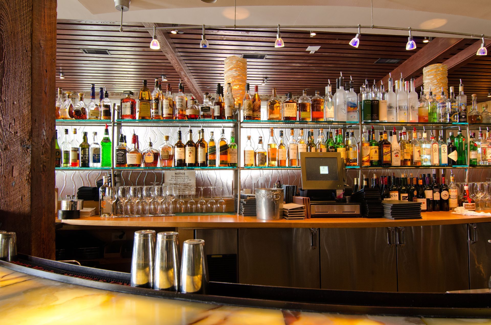 Well-stocked bar with rows of bottles, glasses, and taps under warm lighting