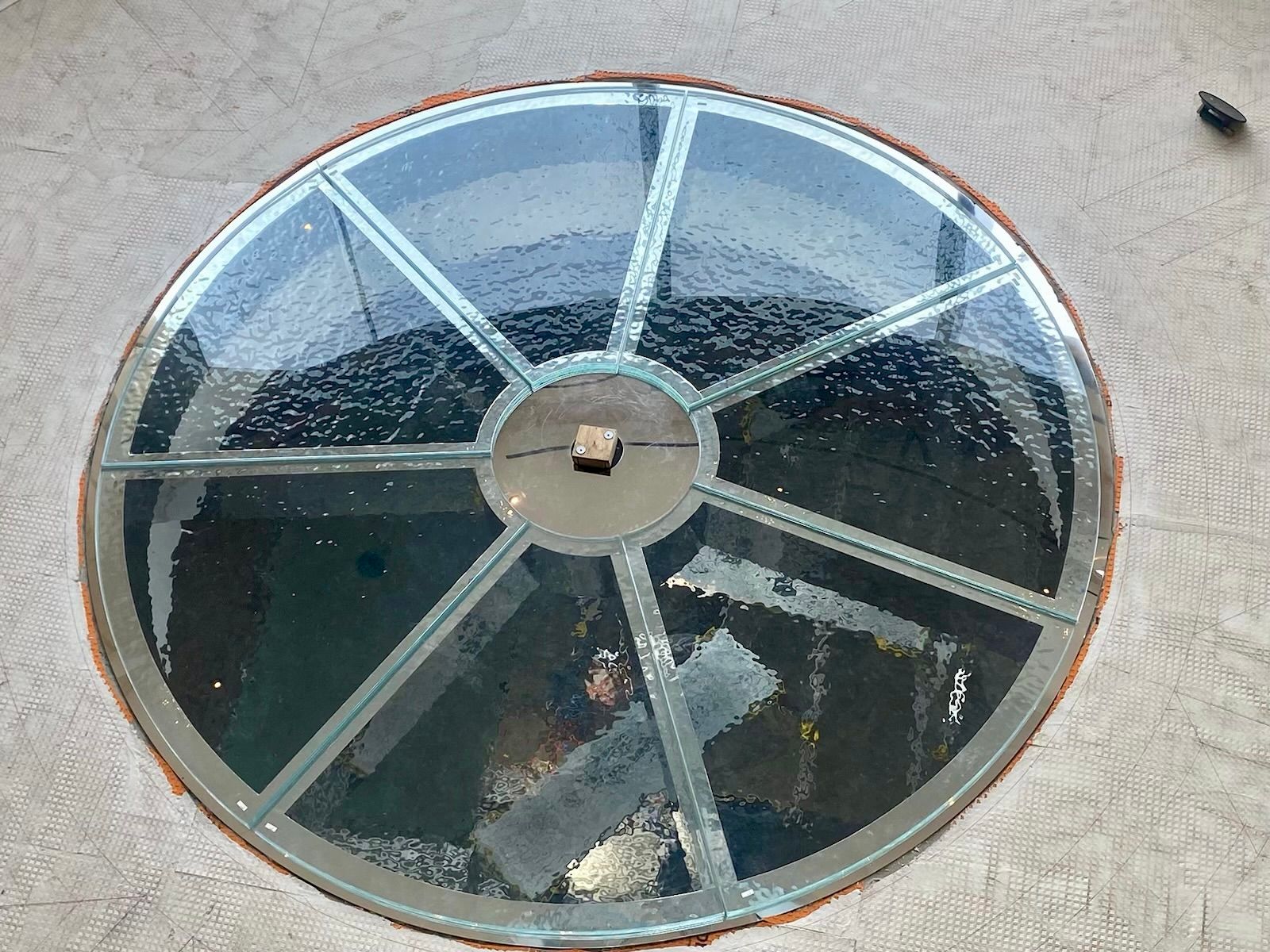 Circular glass floor set in concrete. Interior view with metal framing.