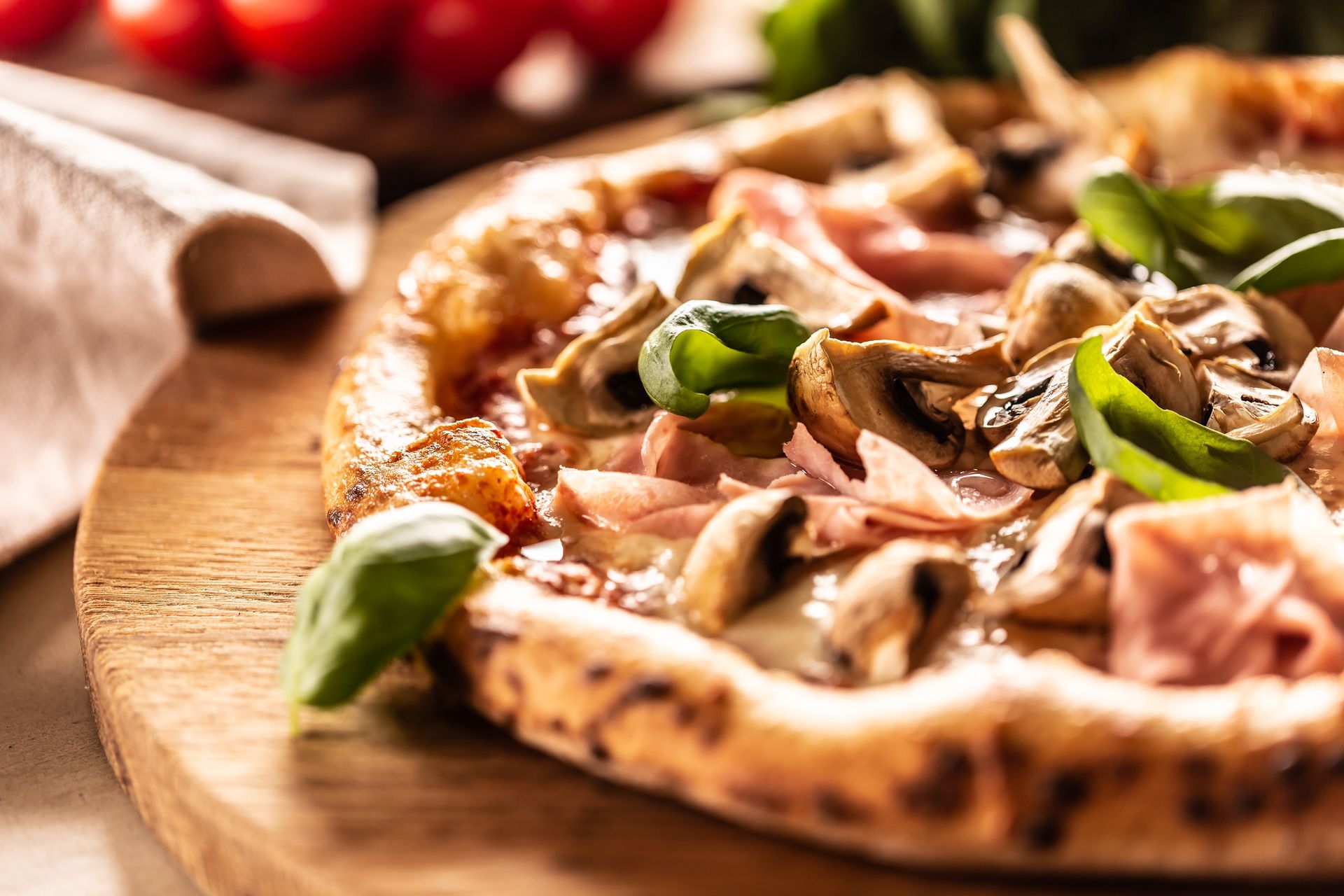 Una pizza cotta nel forno a legna con funghi, prosciutto e foglie di basilico fresco, servita su un rustico tagliere di legno.