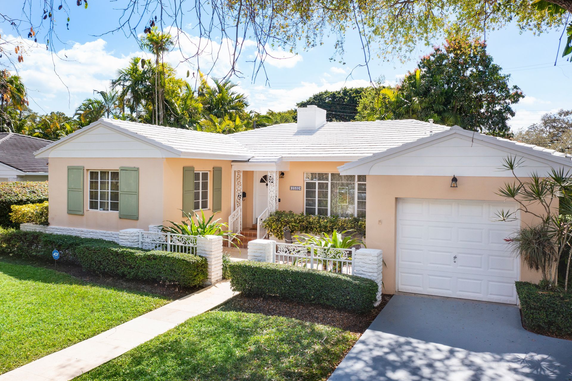 A one-story peach-colored house with a white roof, green shutters, a white garage door, and a manicured front lawn.