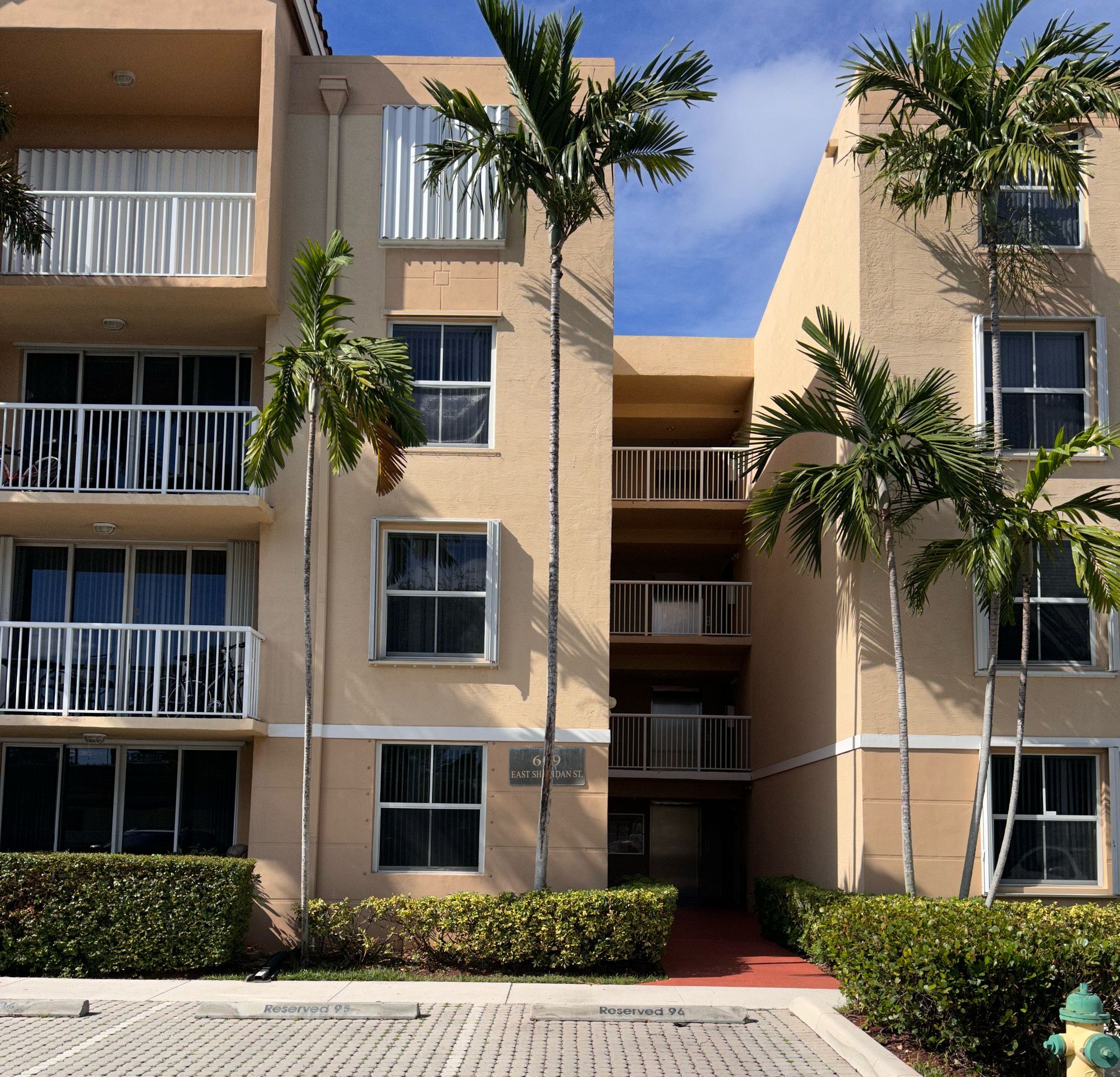 A multi-story beige apartment building with white balconies and palm trees on a sunny day.
