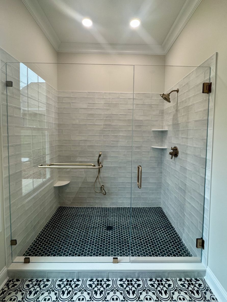 Modern shower with glass doors, white and blue tile, and bronze fixtures.