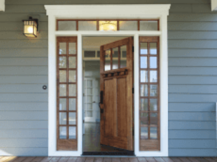 Wooden front door open, flanked by glass panel windows, set in a gray-blue house with white trim in Fayetteville, NC.