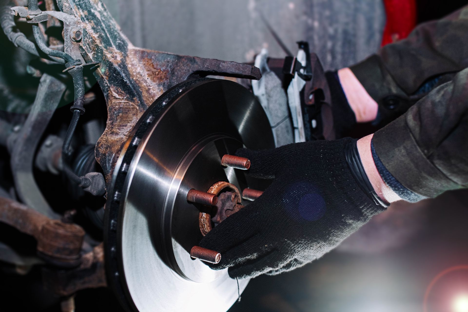 Mechanic in black gloves installs a brake rotor on a car wheel hub.