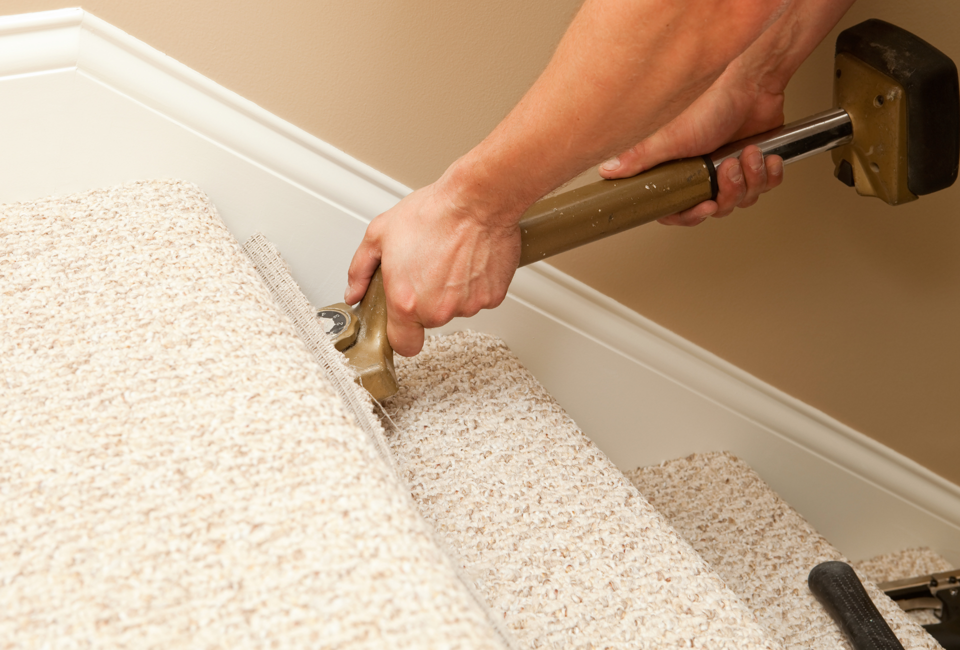 A person is installing carpet on stairs with a hammer.