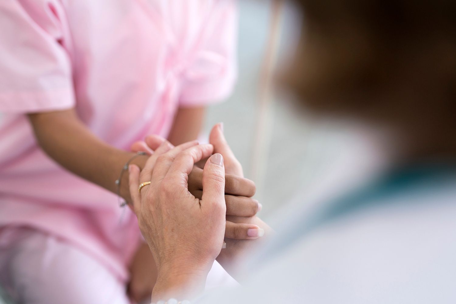 Person in pink scrubs, hands held by another, offering comfort. Person in pink scrubs, hands held by another, offering comfort.
