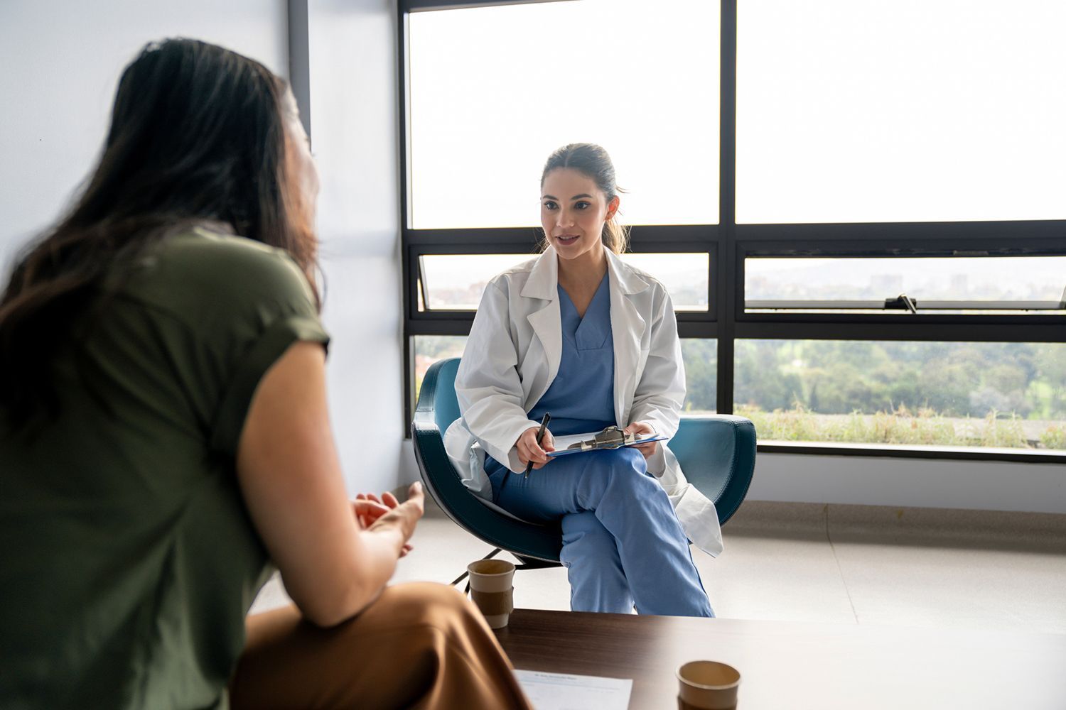 A woman consults with a healthcare professional in a clinic. The professional holds a clipboard. A woman consults with a healthcare professional in a clinic. The professional holds a clipboard.