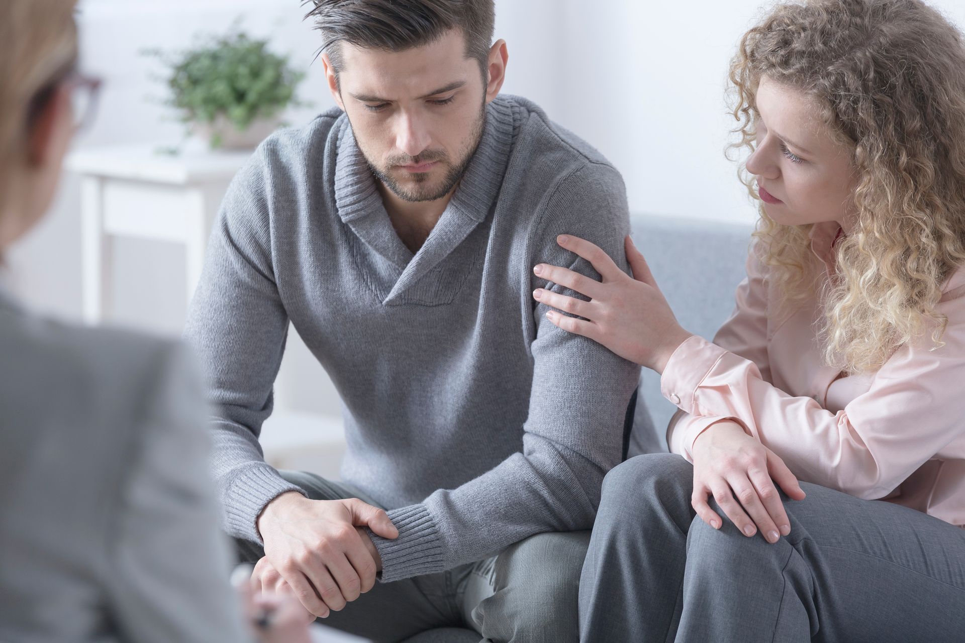 Couple in therapy session, woman comforts man, seated, therapist observes. Couple in therapy session, woman comforts man, seated, therapist observes.