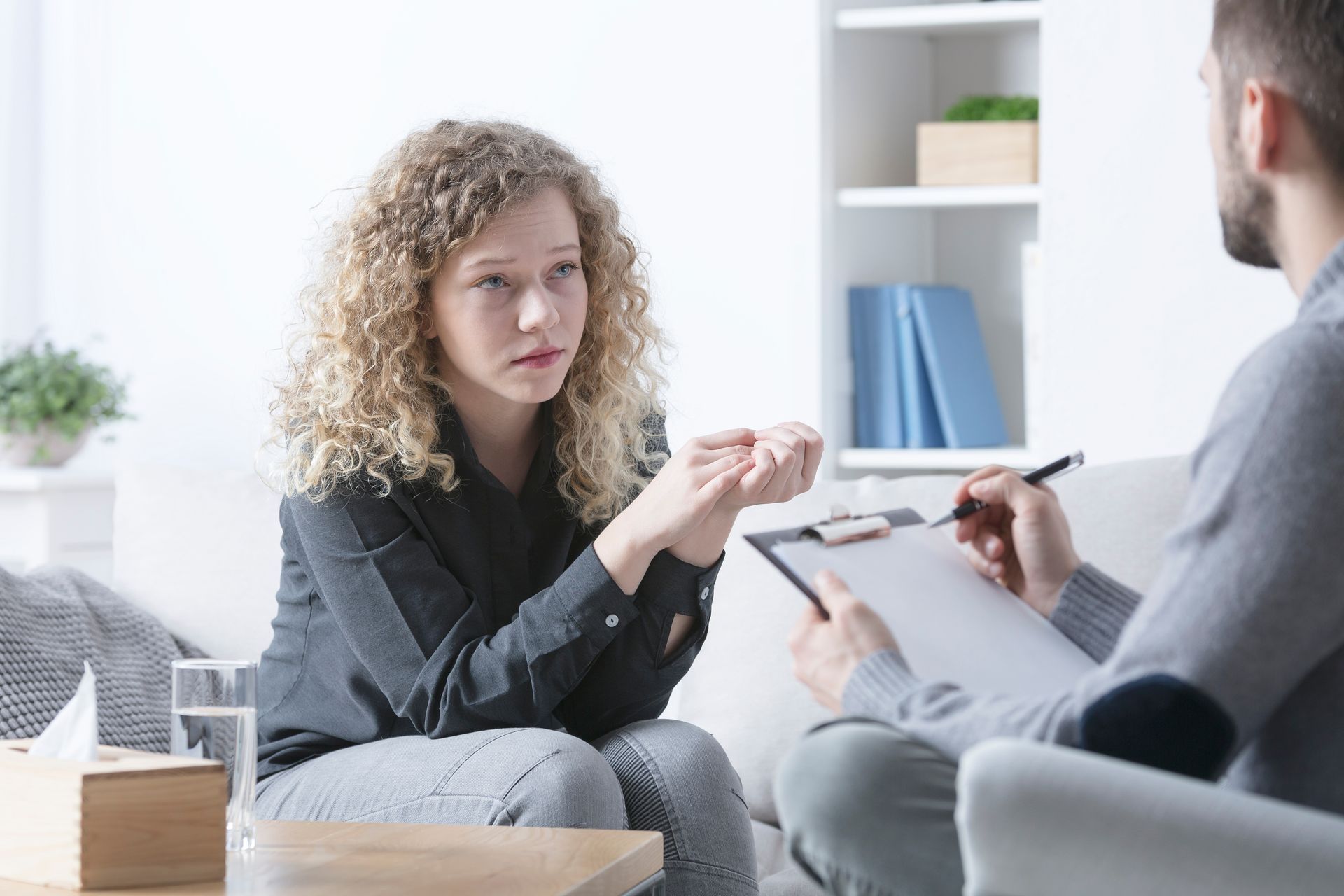 Woman with curly hair talks to a person holding a clipboard in a counseling session.