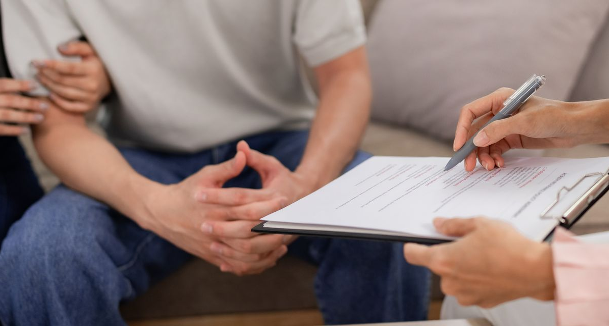 A couple holding hands in therapy session; therapist taking notes on clipboard.