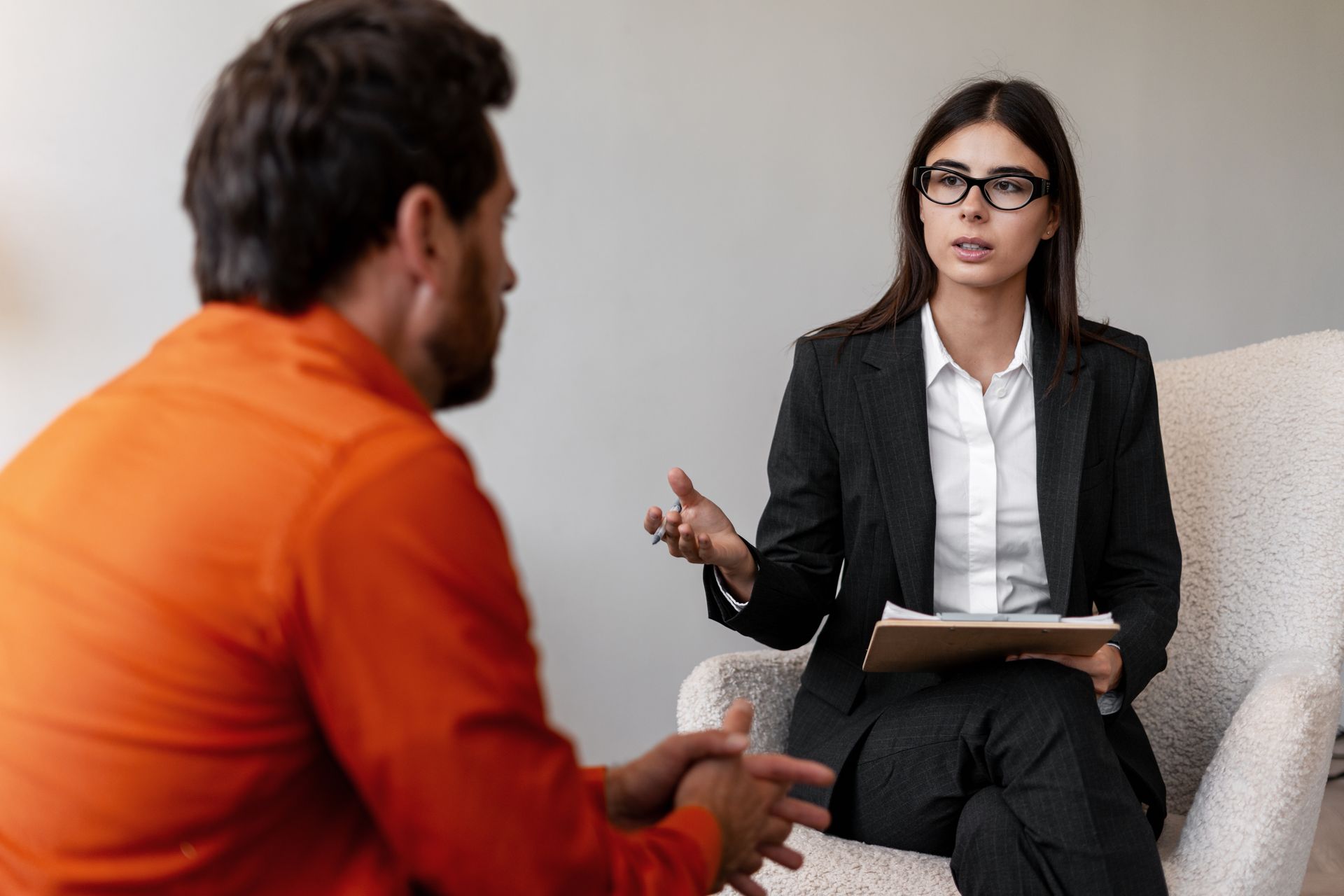 A person in orange is sitting and speaking with a therapist in an office.