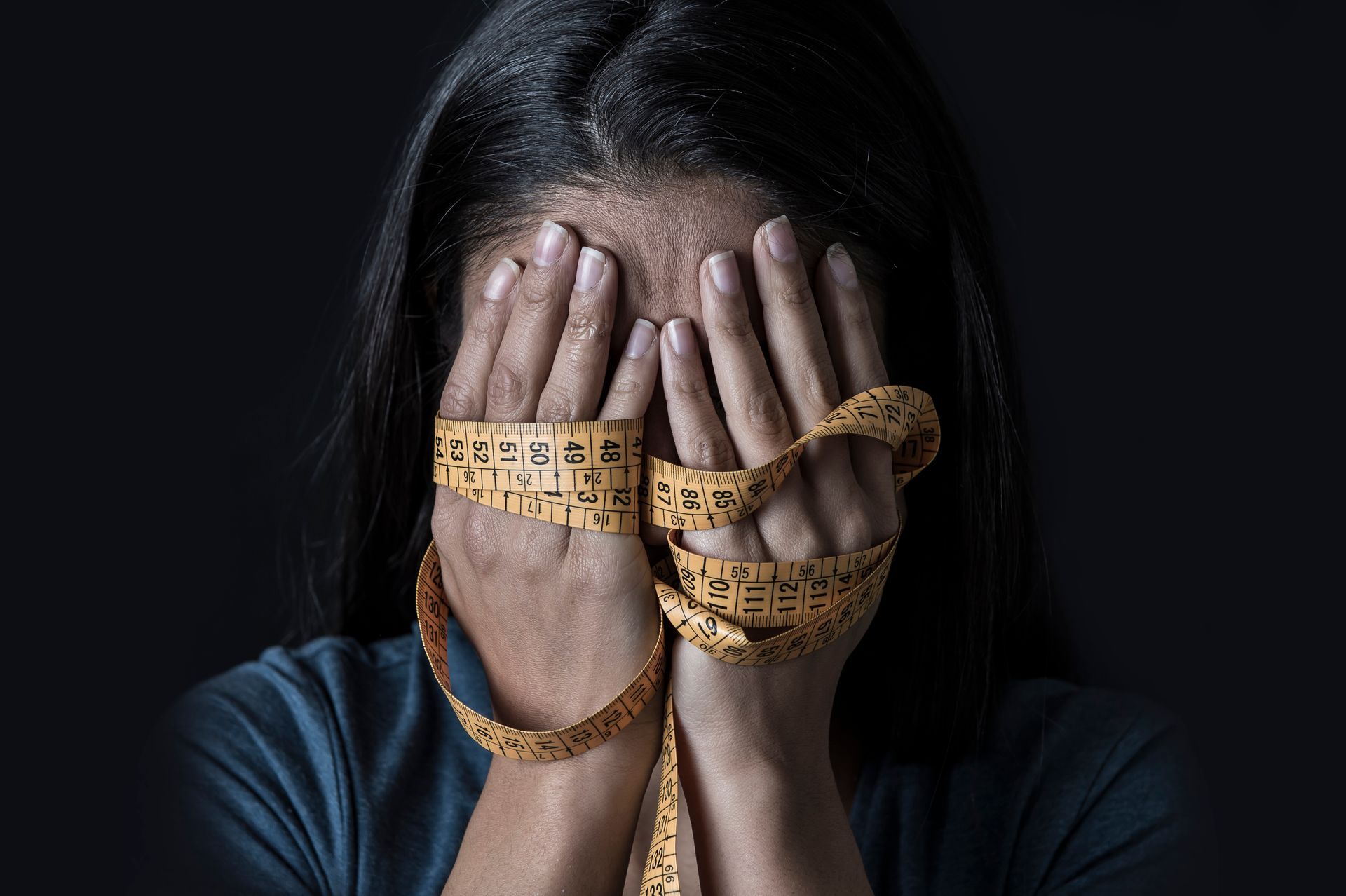 Woman covering face with hands wrapped in measuring tape. Woman covering face with hands wrapped in measuring tape.