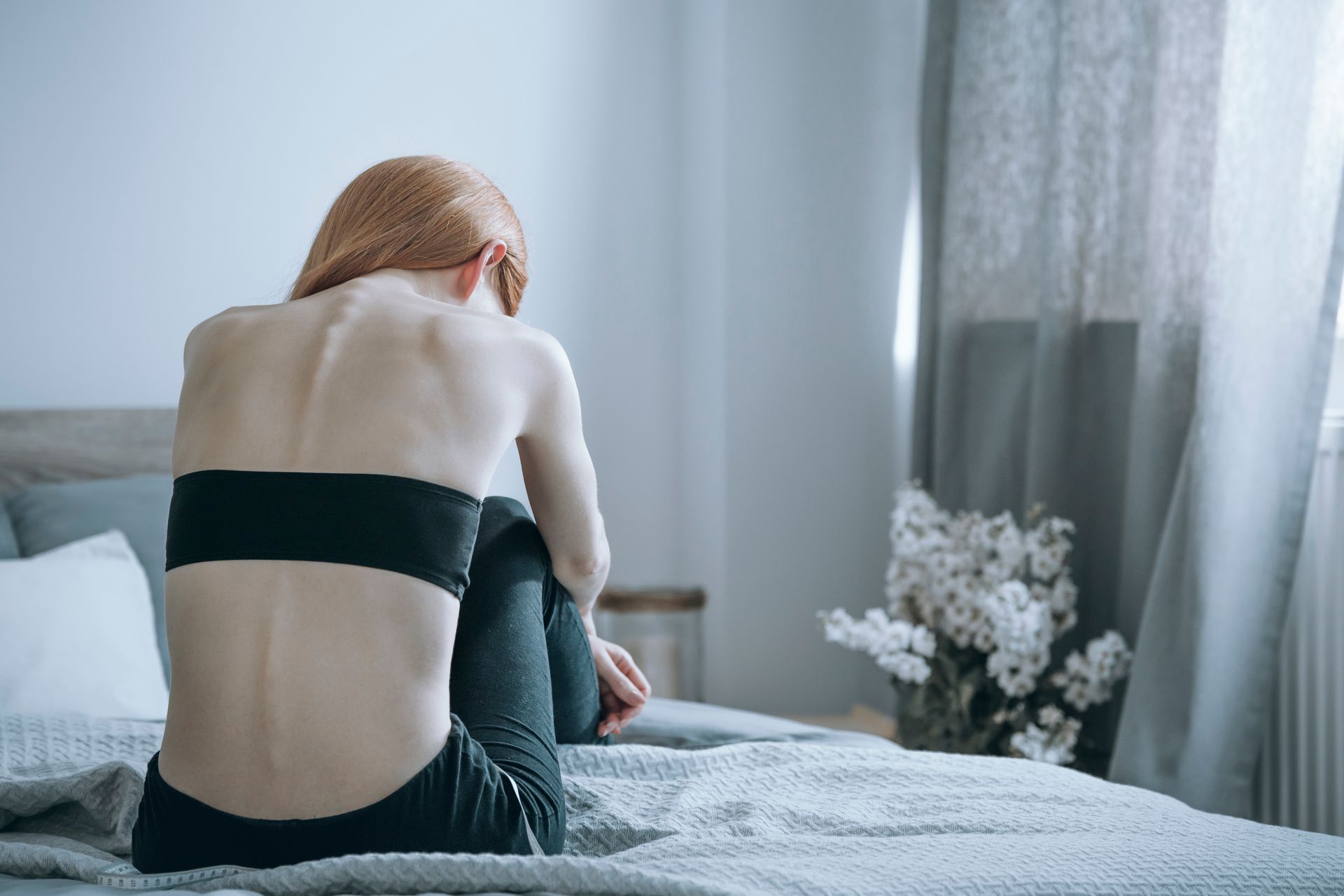 Person with visible ribs sits on bed, facing away. Person with visible ribs sits on bed, facing away.
