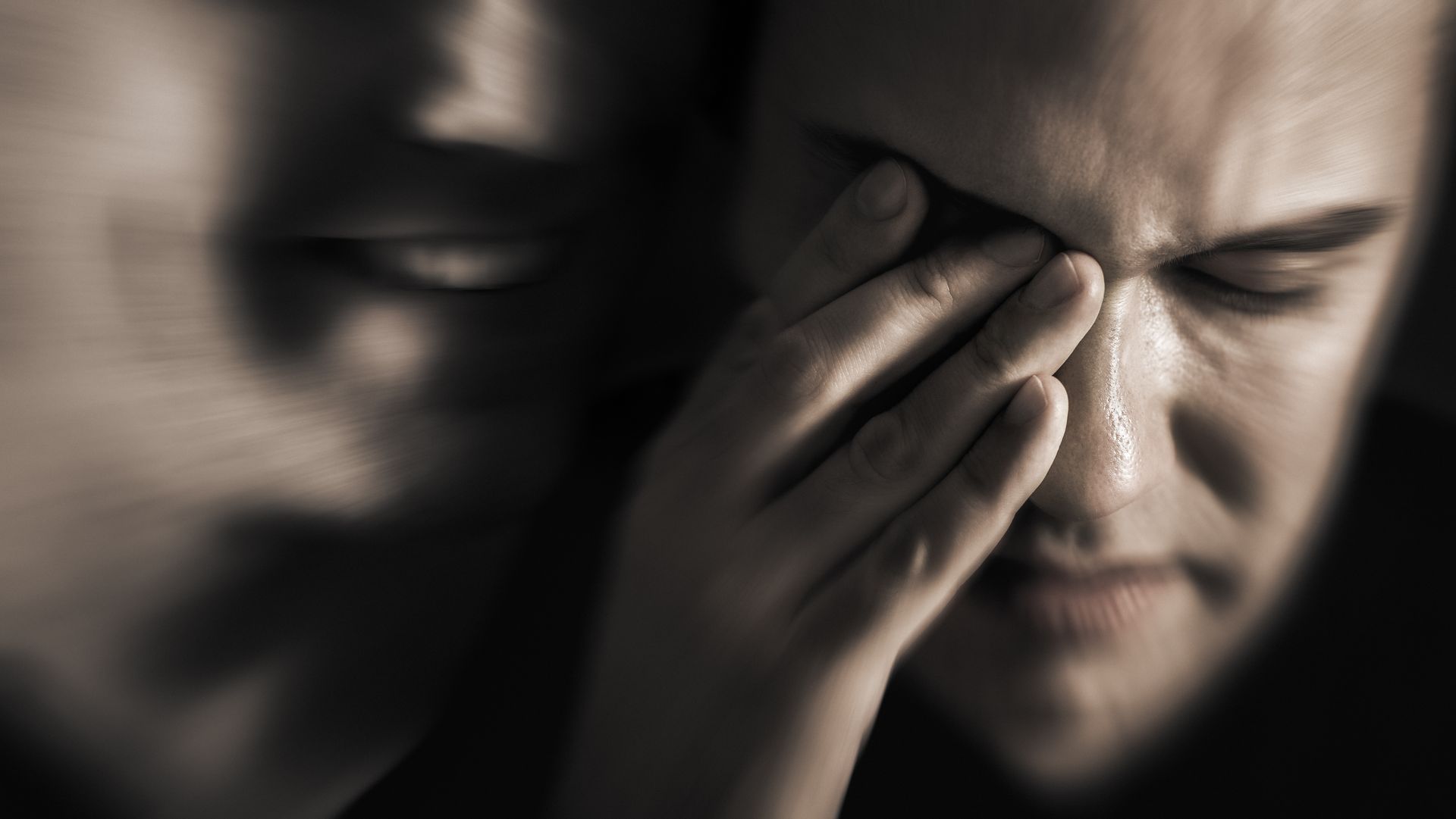 Man with closed eyes, hand on face, appears distressed. Blurred figure to the left. Man with closed eyes, hand on face, appears distressed. Blurred figure to the left.