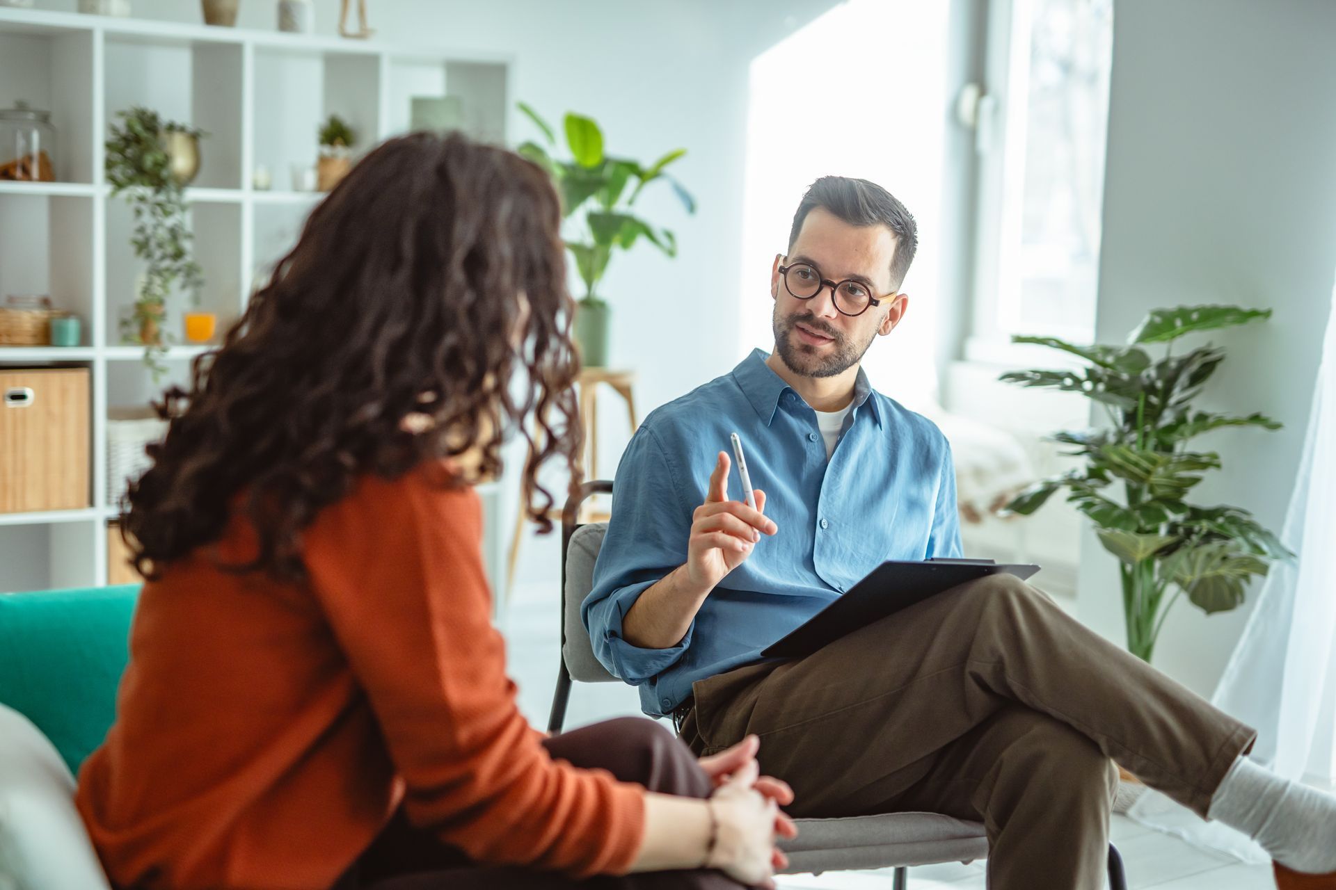 A therapist talking with a person, indoors. The therapist gestures with a finger, holding a tablet. A therapist talking with a person, indoors. The therapist gestures with a finger, holding a tablet.