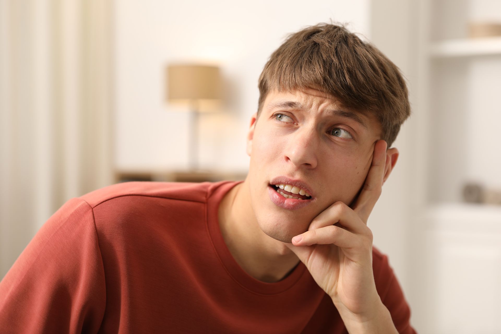 Man in a red shirt looking upwards with a thoughtful expression, hand on his cheek. Man in a red shirt looking upwards with a thoughtful expression, hand on his cheek.