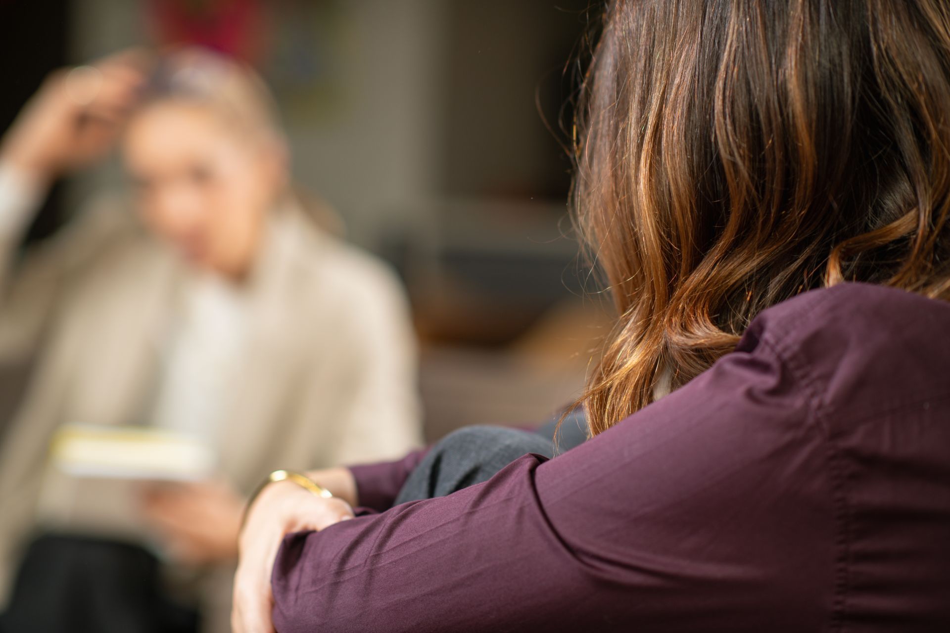 Woman in purple shirt in therapy session, facing therapist who holds notes.