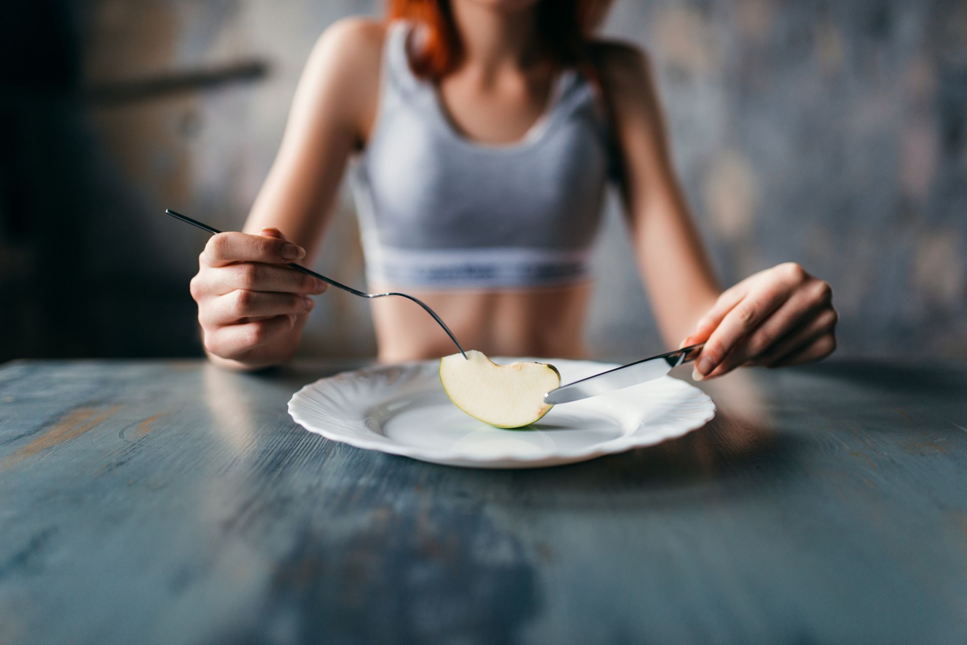 Woman seated at a table with an apple slice on a plate, using a fork and knife. Woman seated at a table with an apple slice on a plate, using a fork and knife.