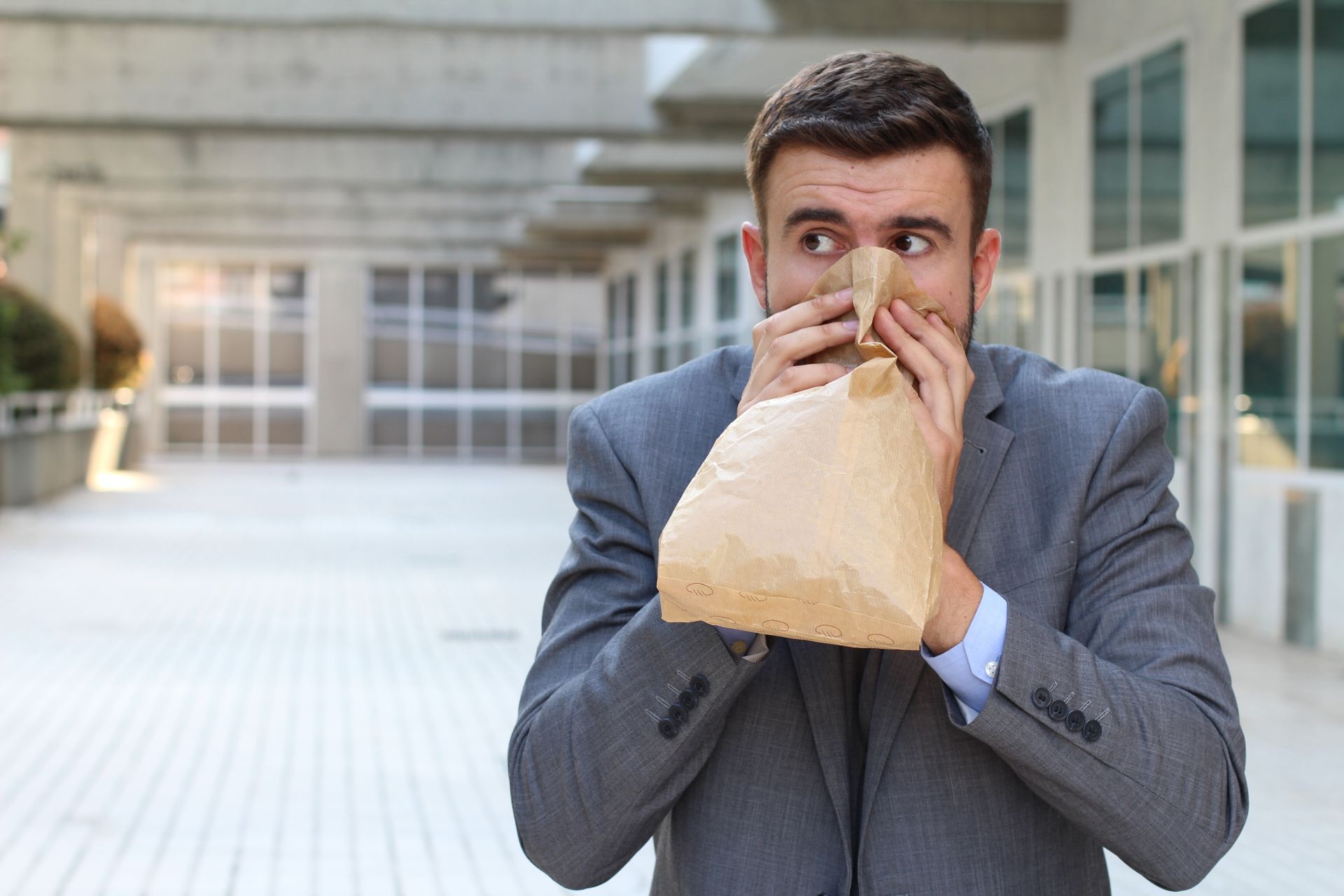Man in suit hyperventilating into a paper bag outside a building. Man in suit hyperventilating into a paper bag outside a building.