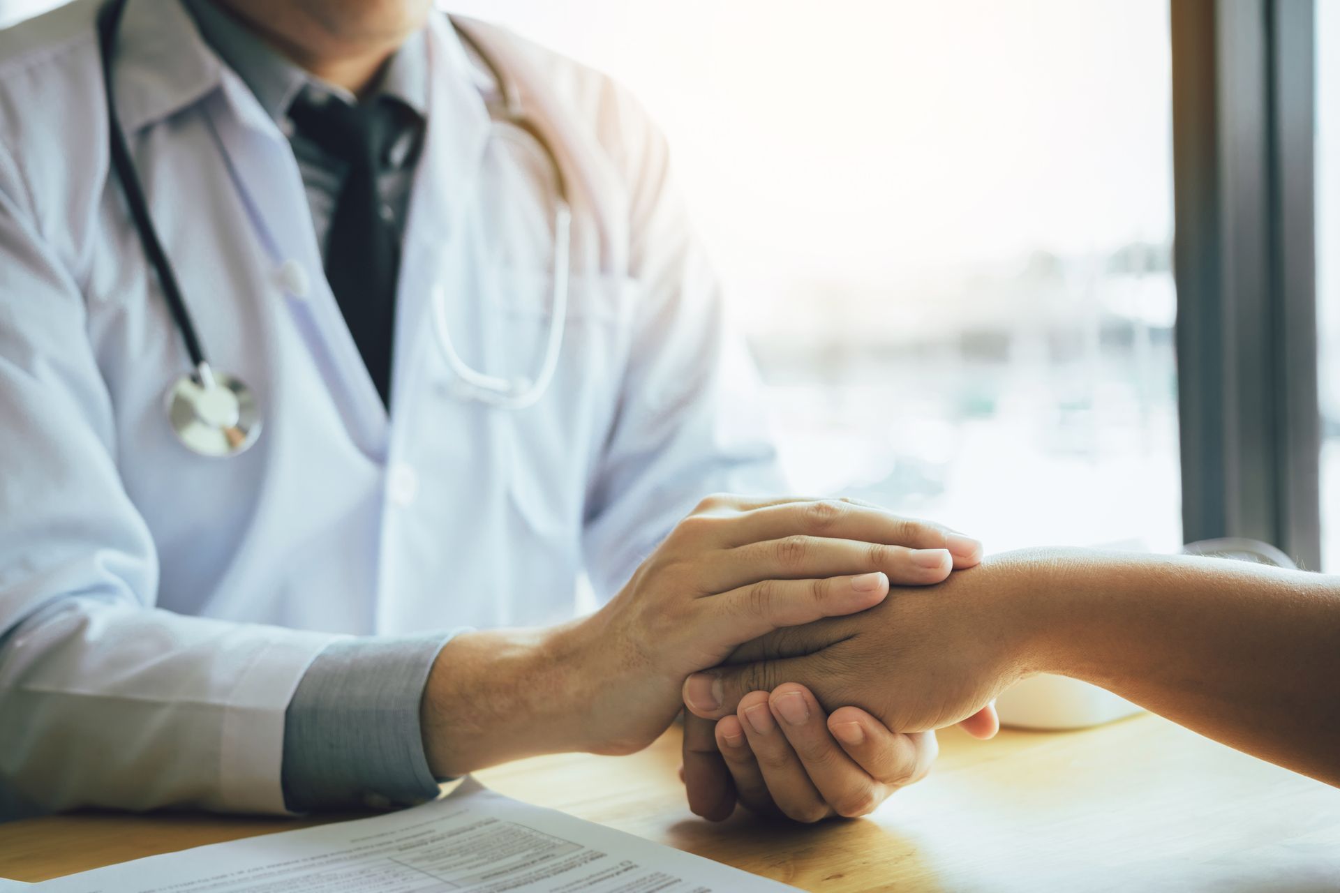 Doctor in white coat holds patient's hand for comfort, in a sunlit room. Doctor in white coat holds patient's hand for comfort, in a sunlit room.