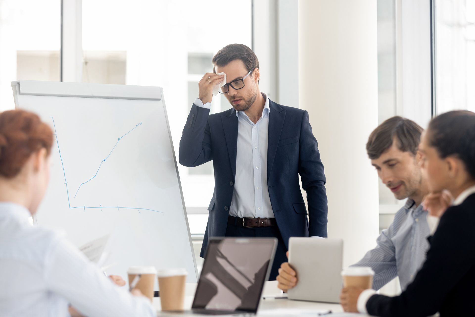 Man sweating while presenting a graph to colleagues in a bright office. Man sweating while presenting a graph to colleagues in a bright office.
