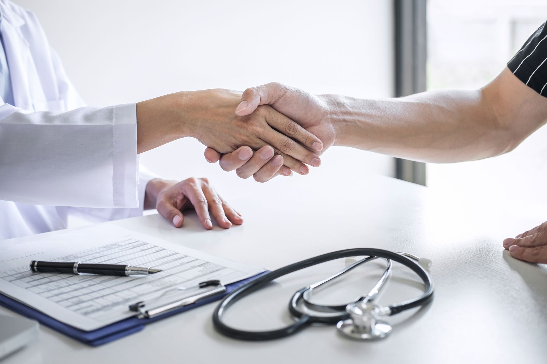 Doctor and patient shaking hands at a desk with medical chart and stethoscope. Doctor and patient shaking hands at a desk with medical chart and stethoscope.