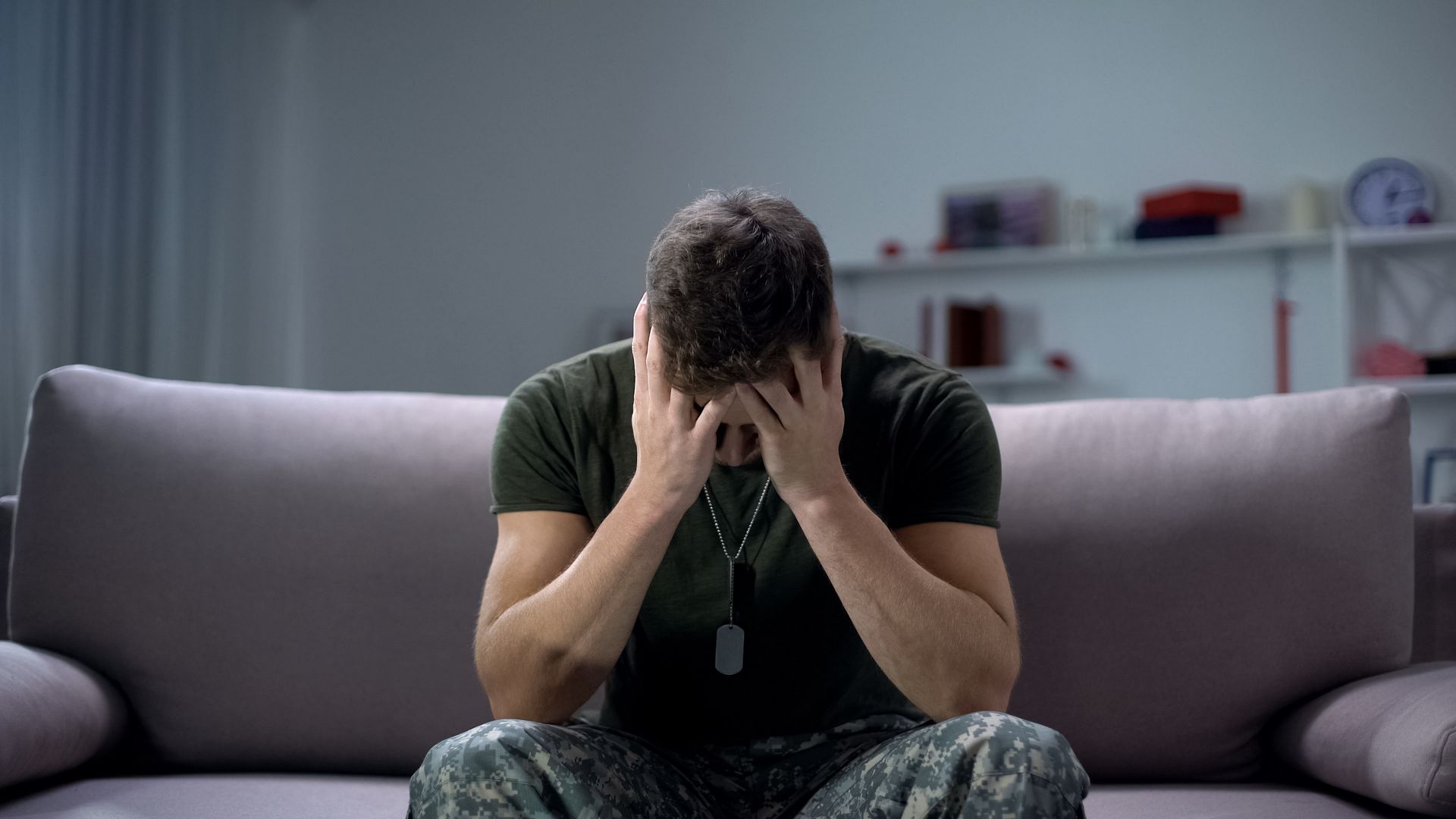 Soldier with head in hands, sitting on couch, appearing distressed. Indoors. Soldier with head in hands, sitting on couch, appearing distressed. Indoors.