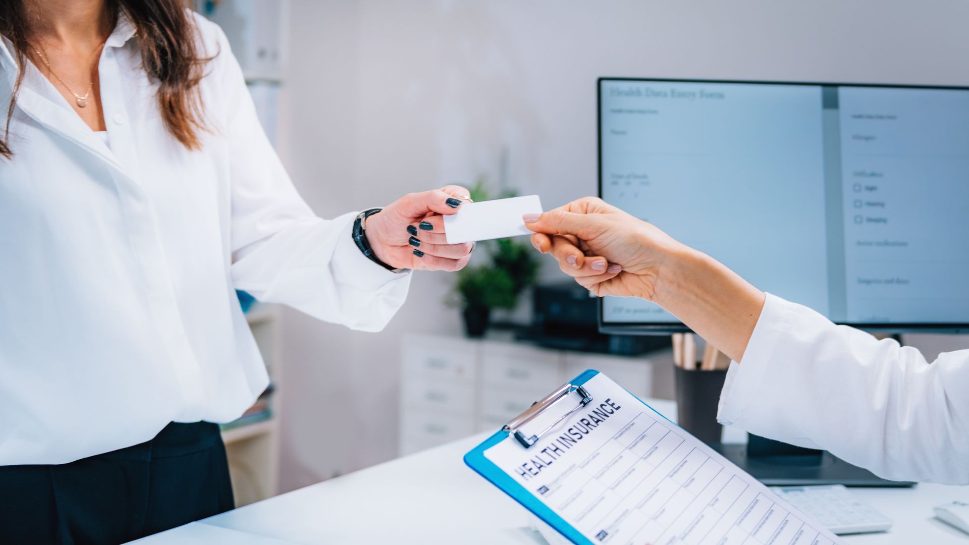 Person in white shirt handing a card to another person behind a desk, healthcare setting.