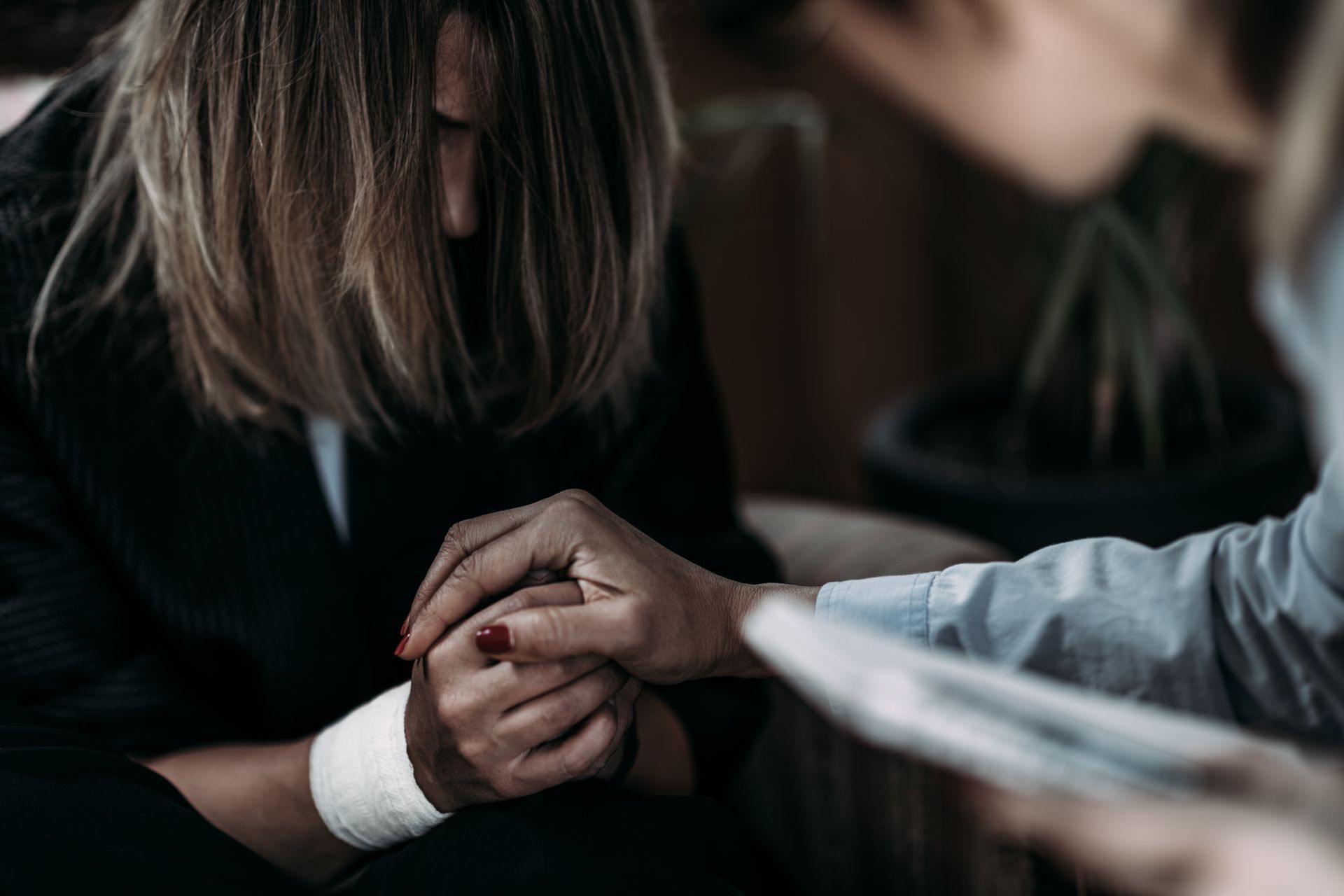 Person comforted by another, holding hands. One person is slumped over, and the other's hand rests on theirs for support. Person comforted by another, holding hands. One person is slumped over, and the other's hand rests on theirs for support.