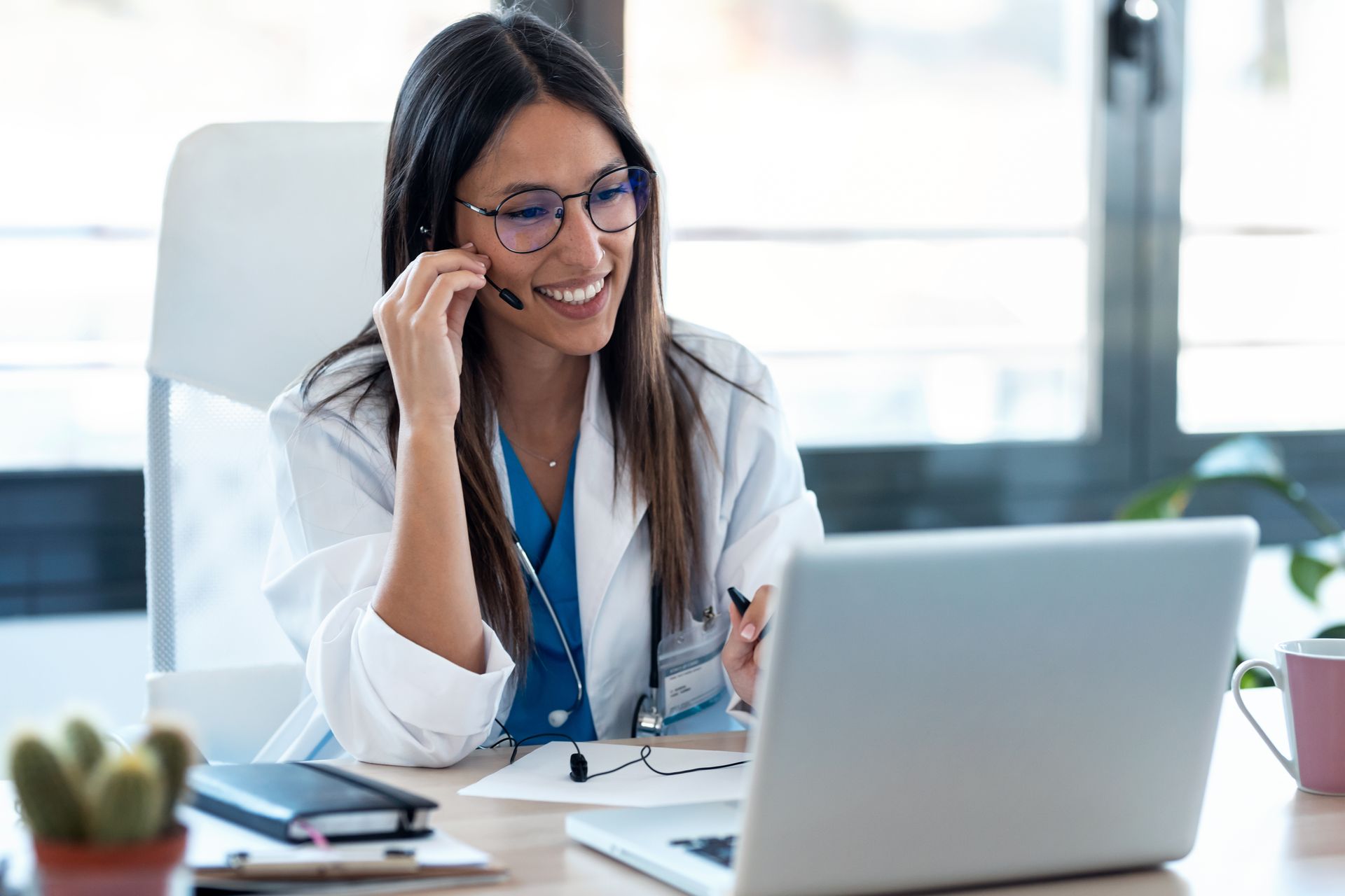 Person in therapy session, seated on a couch, facing therapist in chair; natural light. Smiling doctor on a video call at a desk with a laptop and stethoscope, in a bright office