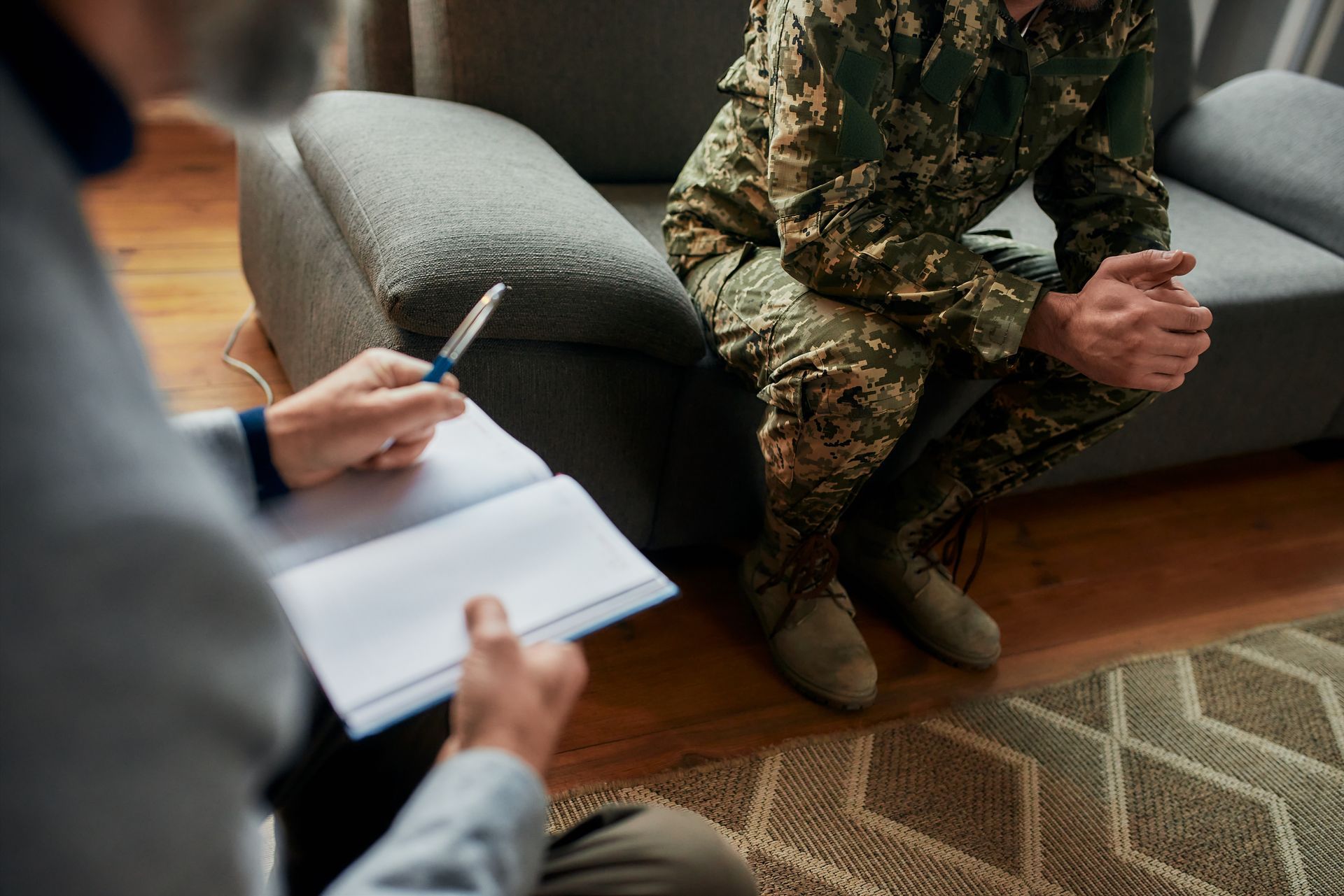 Therapist with notepad and pen; soldier in uniform sits on couch, hands clasped. Counseling session. Therapist with notepad and pen; soldier in uniform sits on couch, hands clasped. Counseling session.