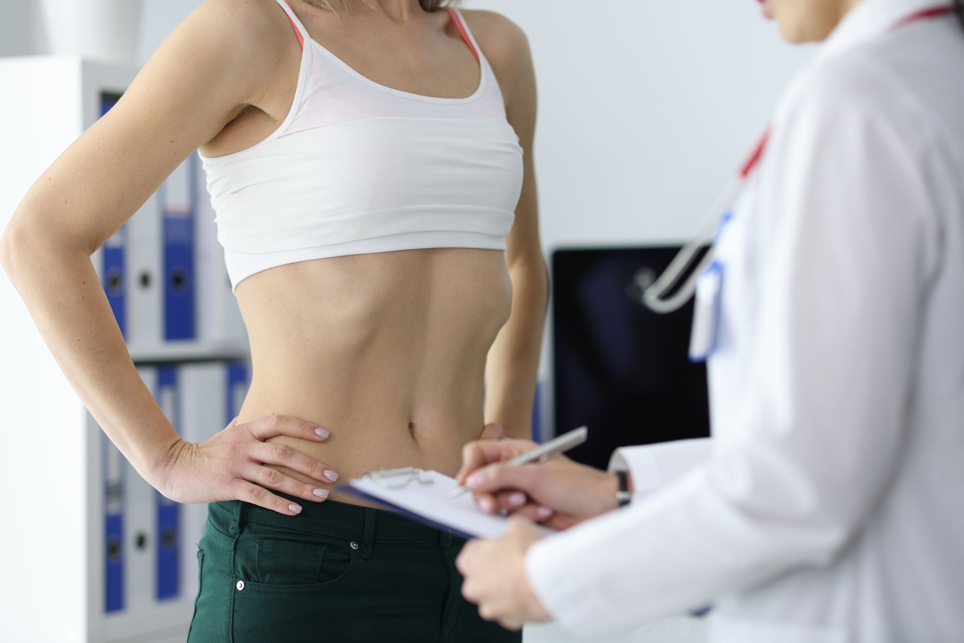 Woman in white top and green pants being examined by a doctor with clipboard in office. Woman in white top and green pants being examined by a doctor with clipboard in office.