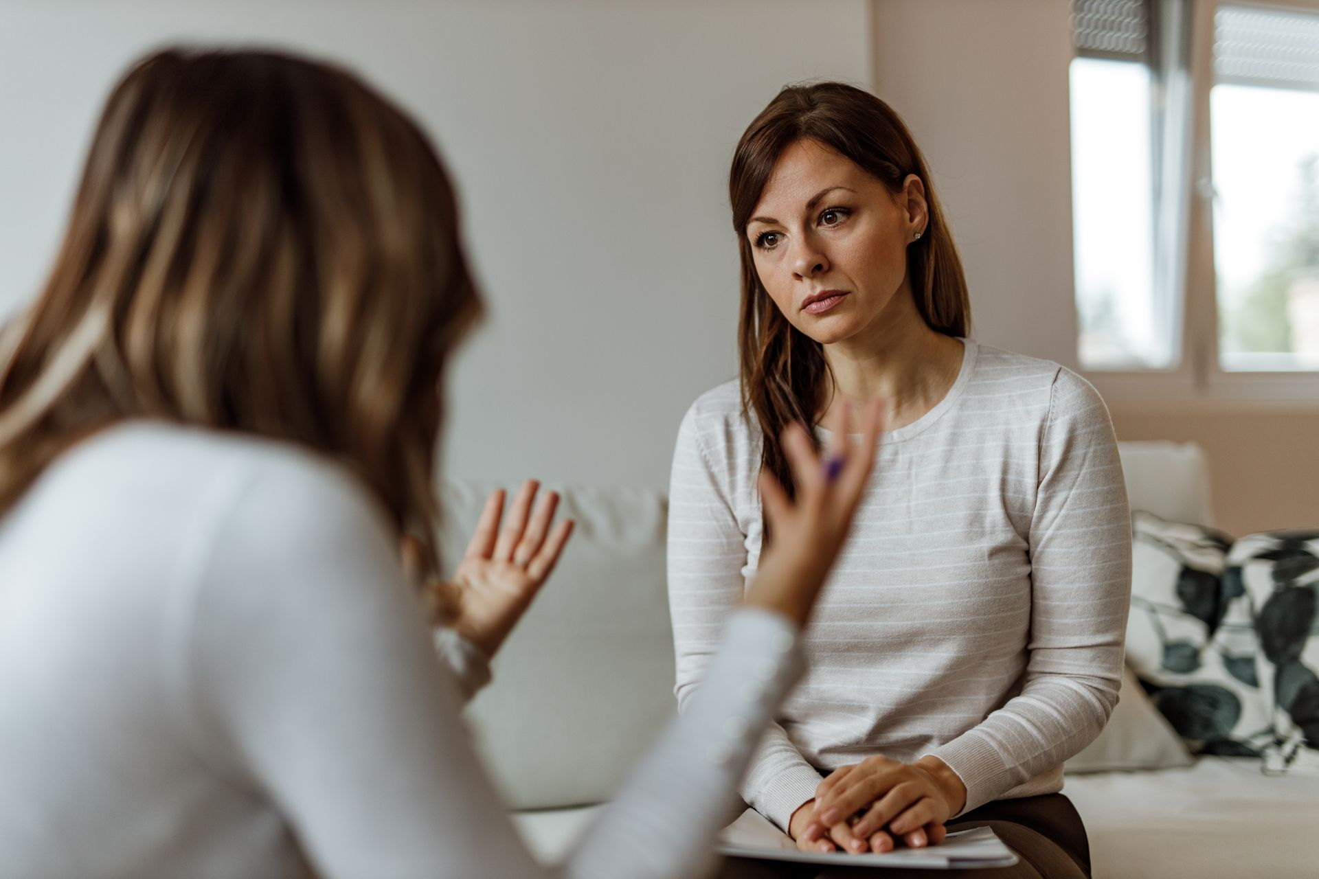 Woman listening to another woman gesturing; soft, natural light, indoors.