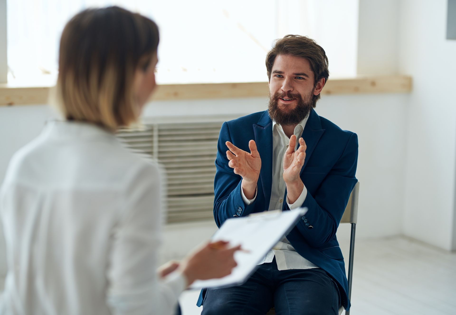 Man in blue jacket clapping, talking to woman holding clipboard, light room. Man in blue jacket clapping, talking to woman holding clipboard, light room.