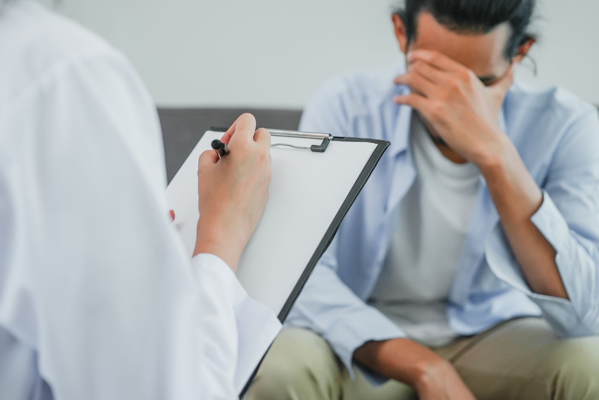 Person in distress seated during a session with a medical professional taking notes. Person in distress seated during a session with a medical professional taking notes.