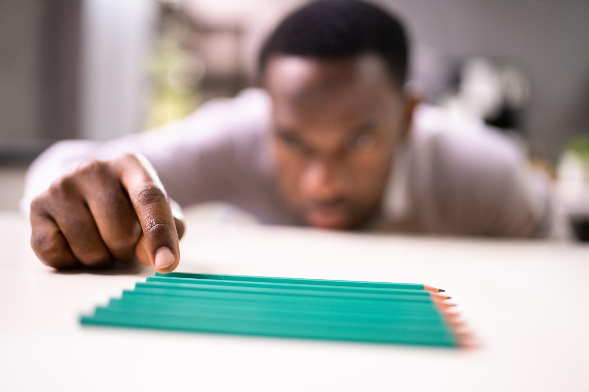 Person focused on a row of green pencils on a table, pointing with one finger.